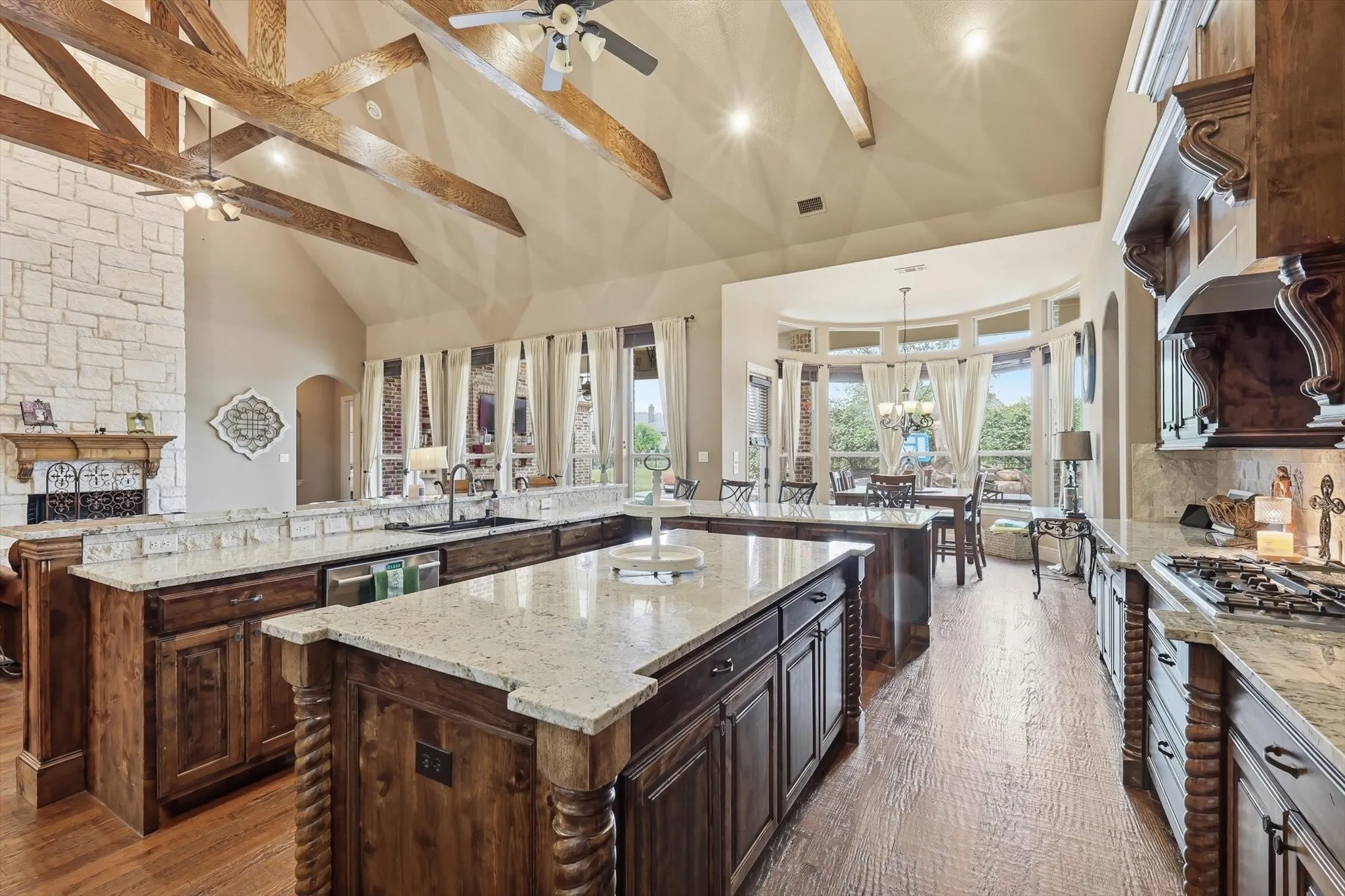 Kitchen with dark wood finish cabinets, arched walkways, open floor plan, light stone countertops, and vaulted ceiling
