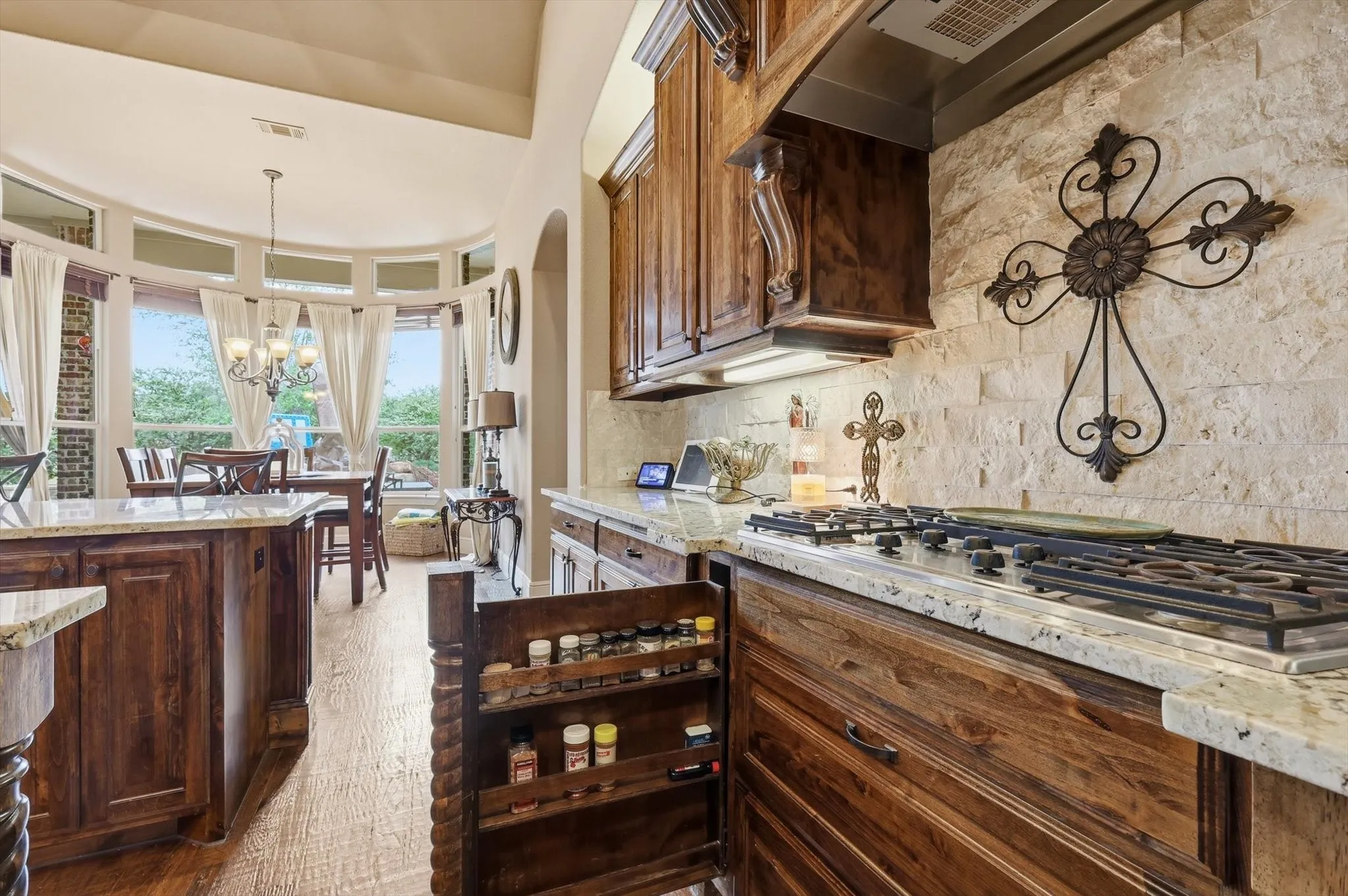 Kitchen featuring light stone counters, stainless steel gas cooktop, tasteful backsplash, light wood-style flooring, and arched walkways