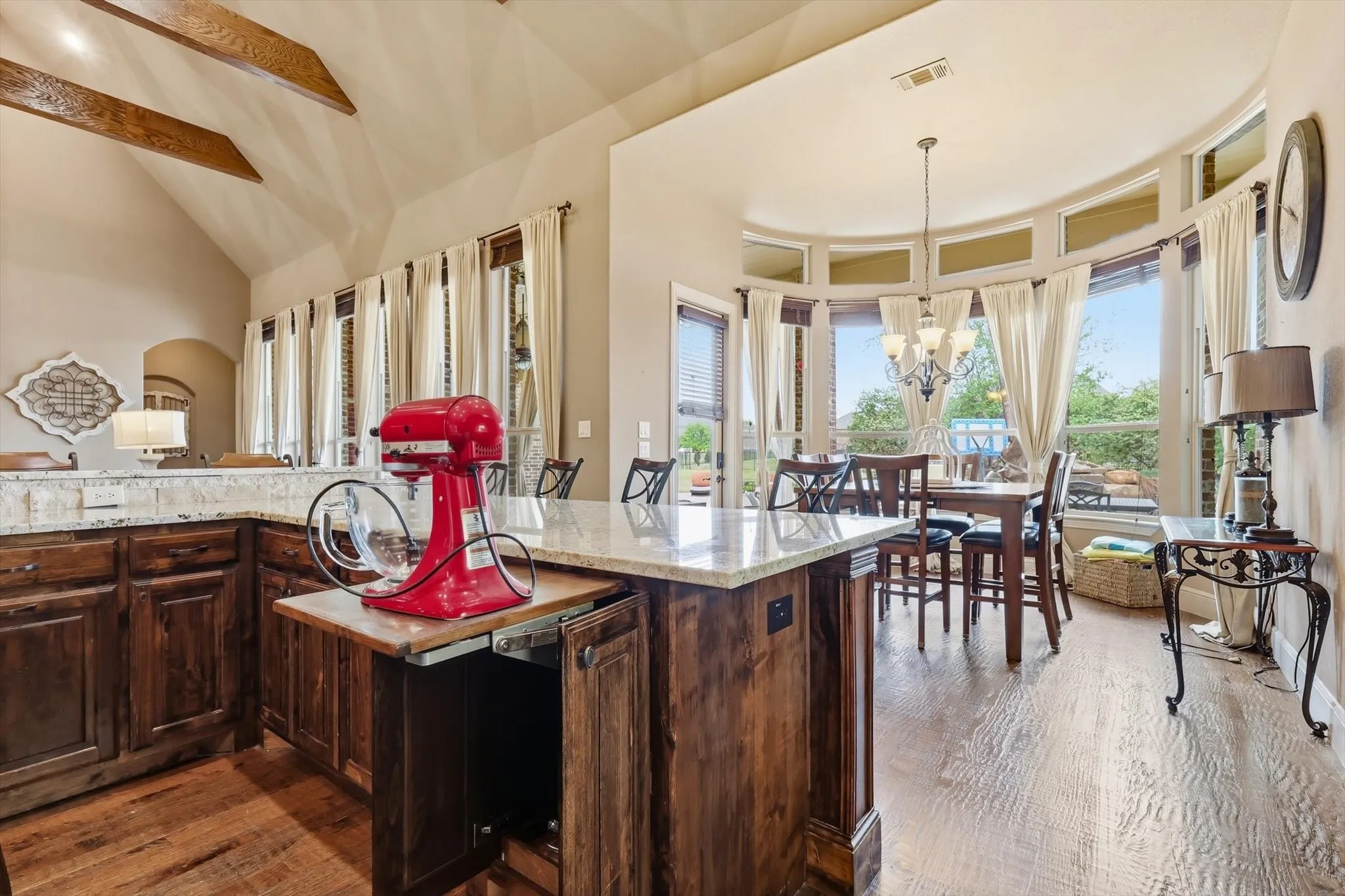 Kitchen featuring dark wood finish cabinetry, dark wood-style floors, light stone counters, a chandelier, and healthy amount of natural light