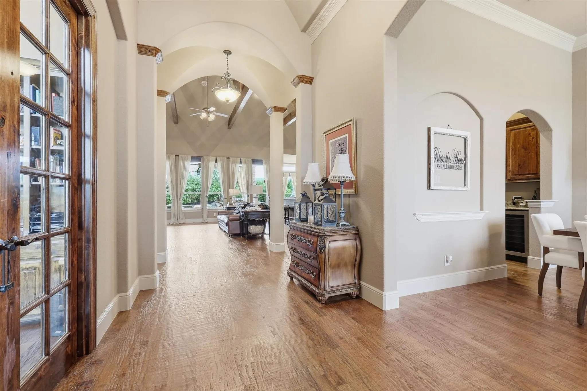 Hallway with arched walkways, light wood-style flooring, beverage cooler, vaulted ceiling, and crown molding