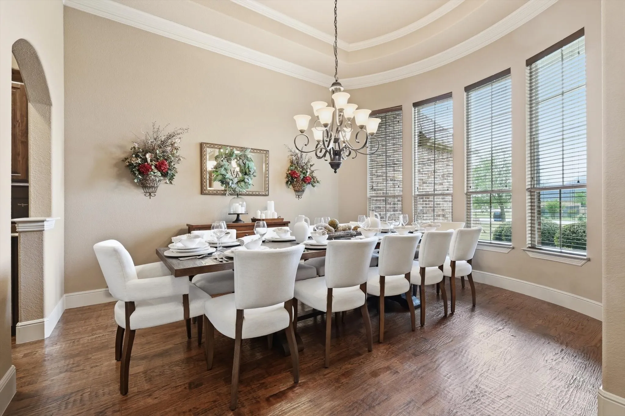 Dining space with ornamental molding, dark wood finished floors, a chandelier, a raised ceiling, and arched walkways