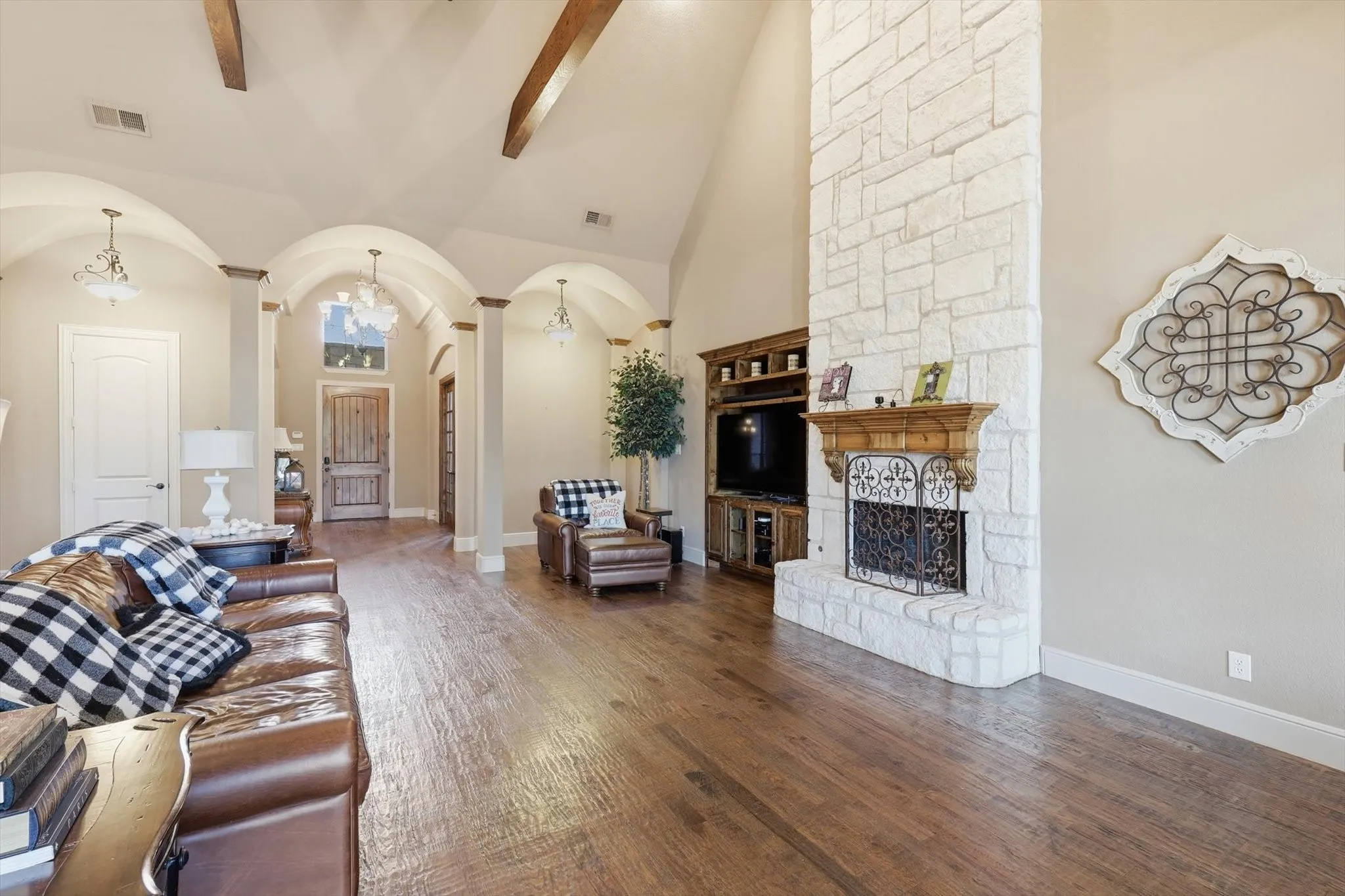 Living area featuring arched walkways, a stone fireplace, hardwood / wood-style floors, and vaulted ceiling