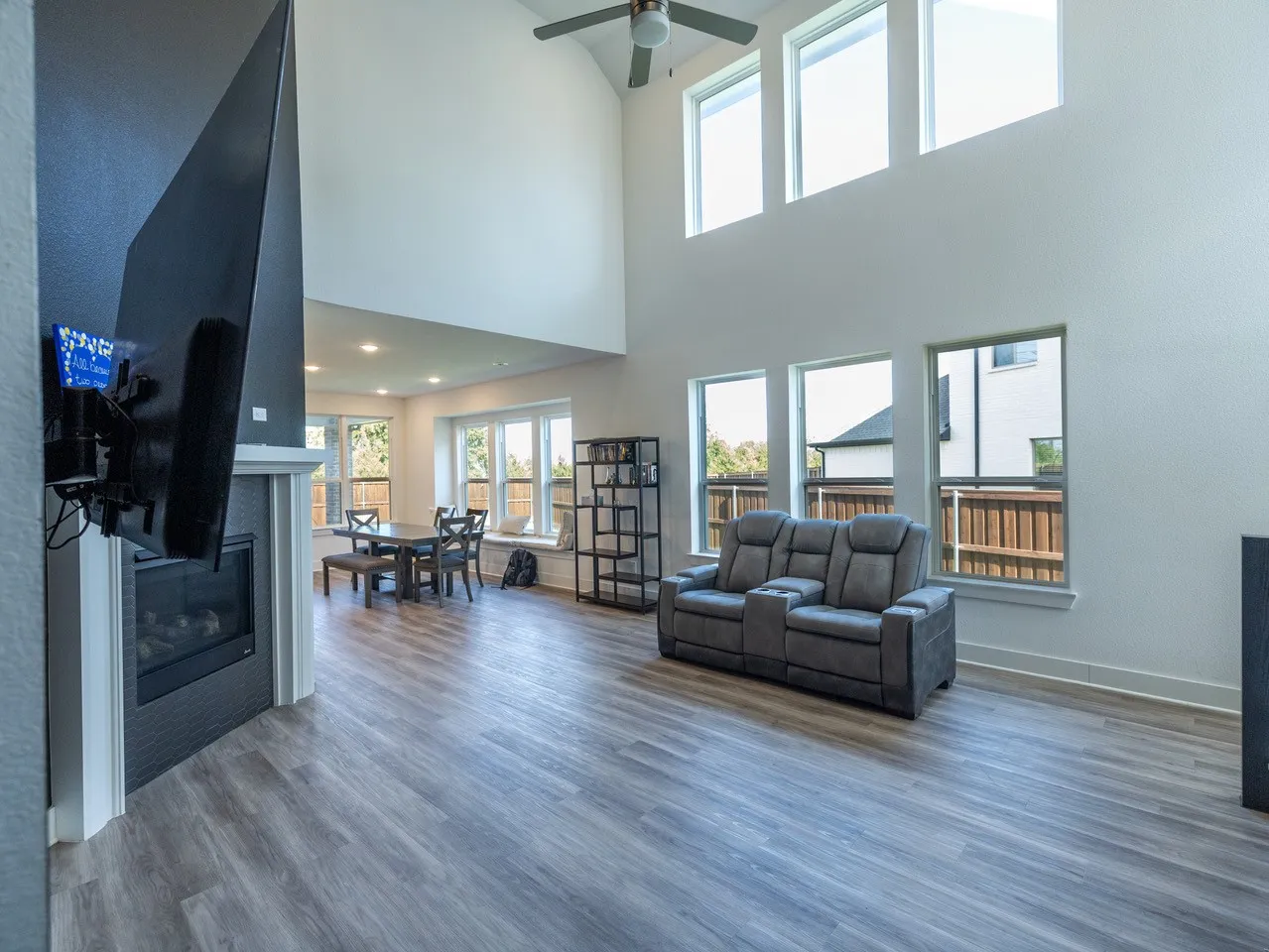 Two-story great room featuring a gas fireplace with a tiled surround, high vaulted ceilings, wood-finish flooring, and multiple large windows