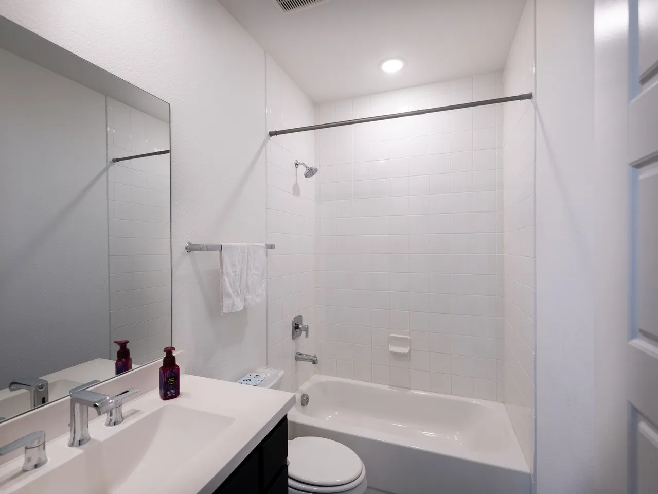 White subway tile shower surround, chrome fixtures, built-in bathtub, recessed ceiling lighting, and a vanity with an integrated sink