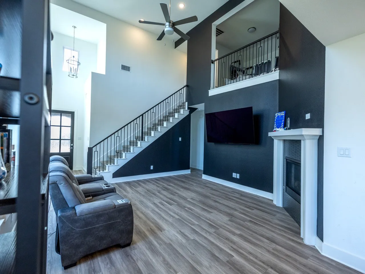 Vaulted ceilings with a ceiling fan, a fireplace with a white mantel, an interior balcony with black metal railings, and wood-finish flooring