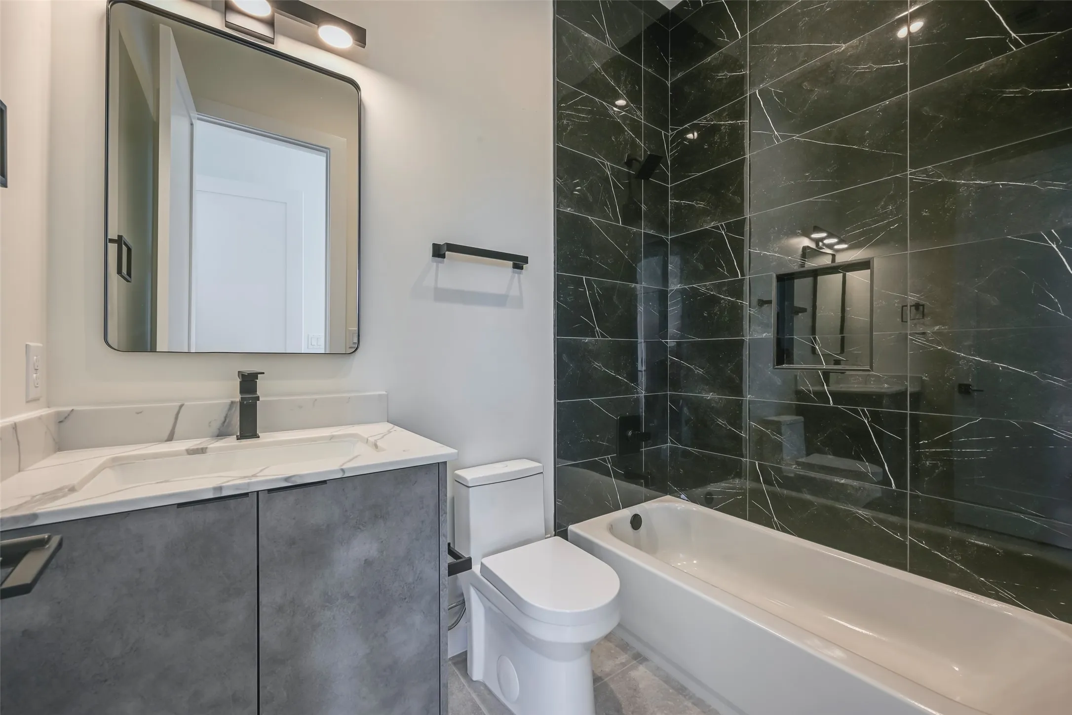 Bathroom featuring a white vanity with an integrated sink, matte black faucet, and a rectangular mirror with overhead lighting