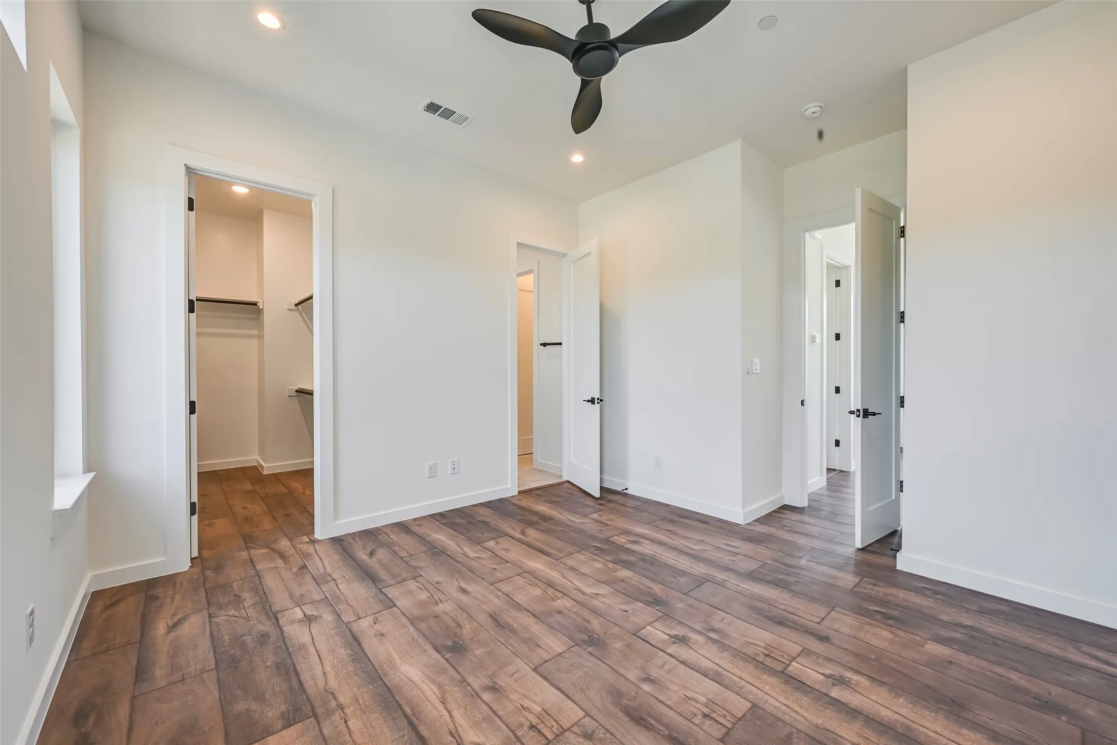 Spacious room featuring wood-finish flooring, a modern black ceiling fan, recessed lighting, and a walk-in closet with shelving and hanging rods
