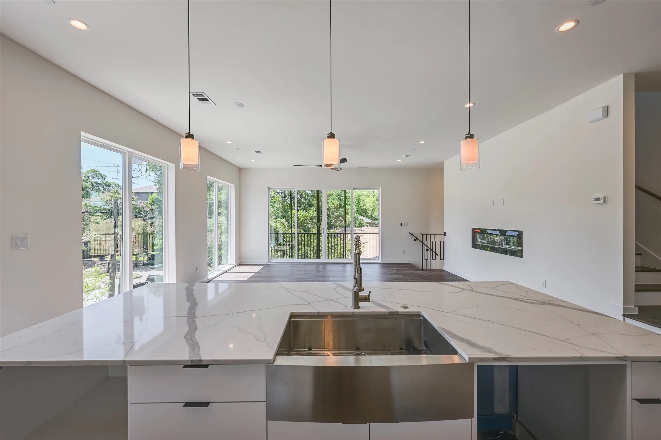 White kitchen island with a stainless steel farmhouse sink and contemporary pendant lighting