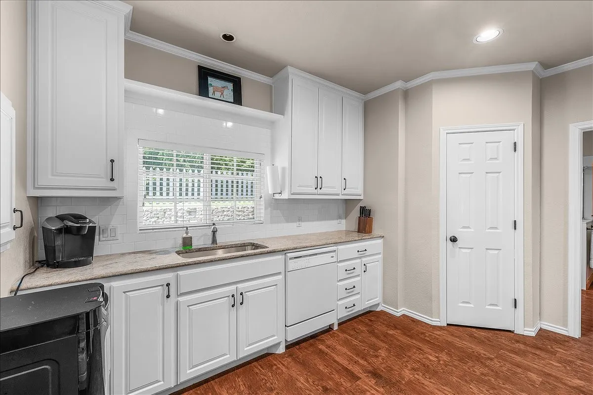 Kitchen featuring light stone counters, white cabinets, black microwave, crown molding, and white dishwasher