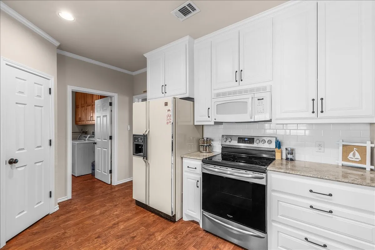 Kitchen with white appliances, white cabinets, crown molding, dark wood-type flooring, and light stone countertops