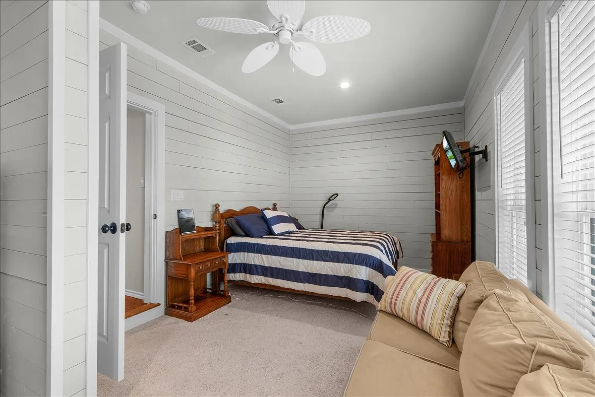Bedroom with carpet, wooden walls, crown molding, and ceiling fan