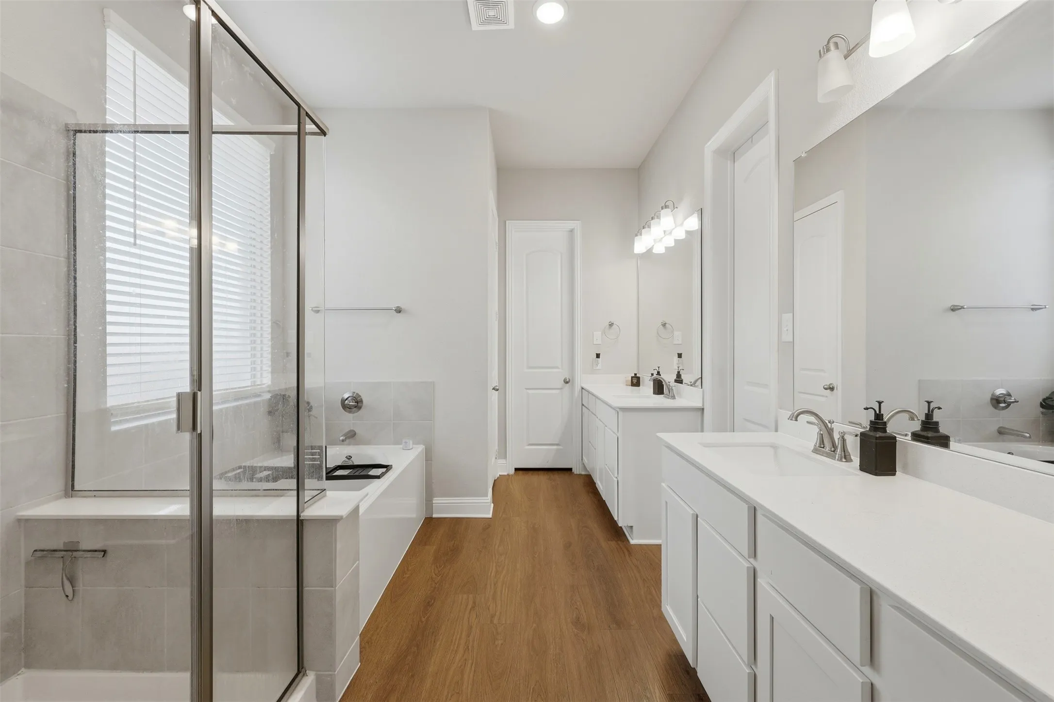 Bathroom featuring two vanities, a bath, a shower stall, and dark wood finished floors