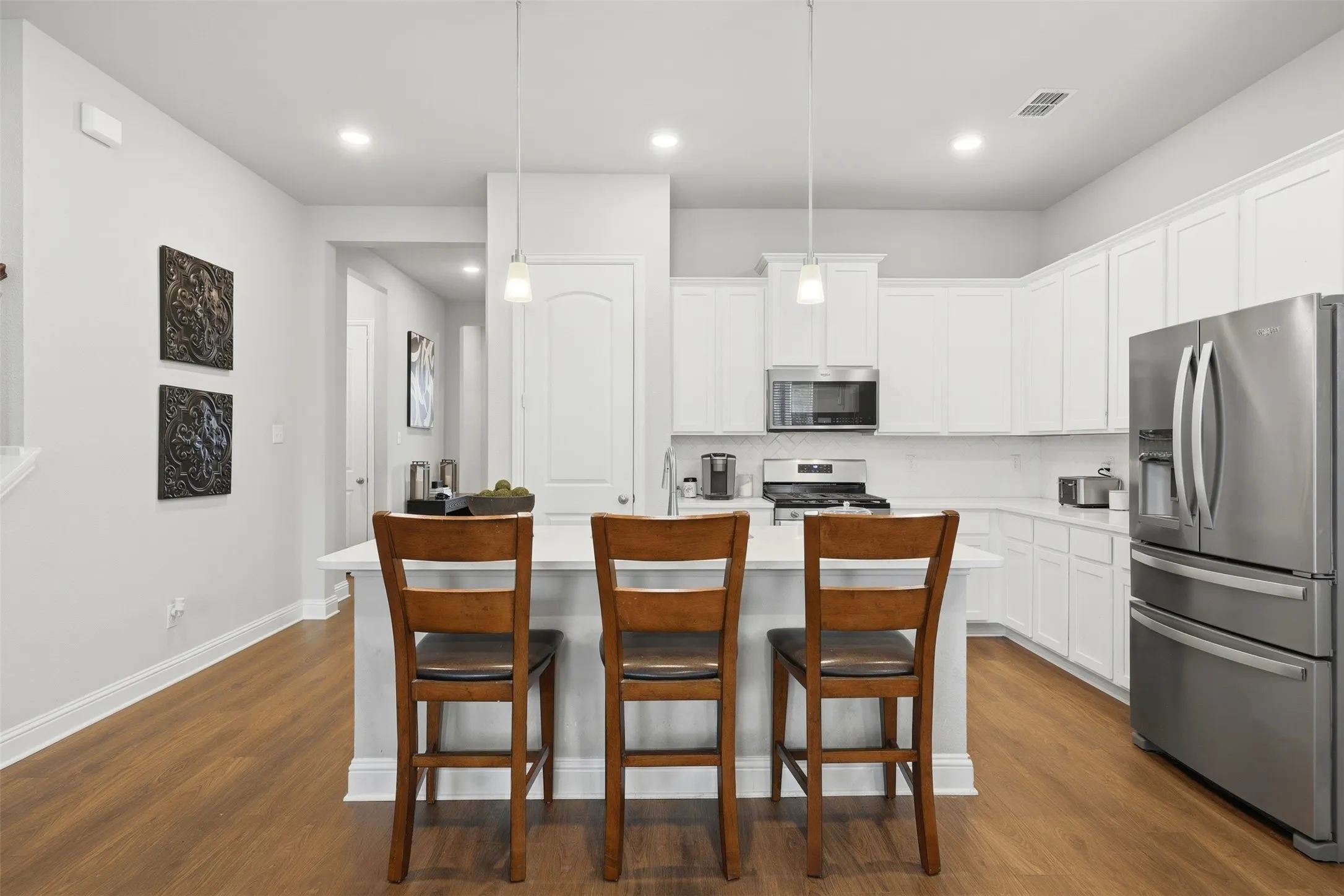 Kitchen with stainless steel appliances, a kitchen island with sink, a breakfast bar, decorative backsplash, and white cabinets