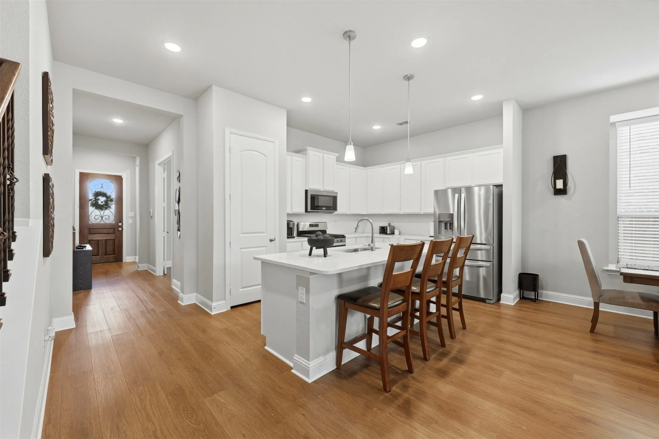 Kitchen featuring a kitchen bar, stainless steel appliances, white cabinetry, a kitchen island with sink, and pendant lighting