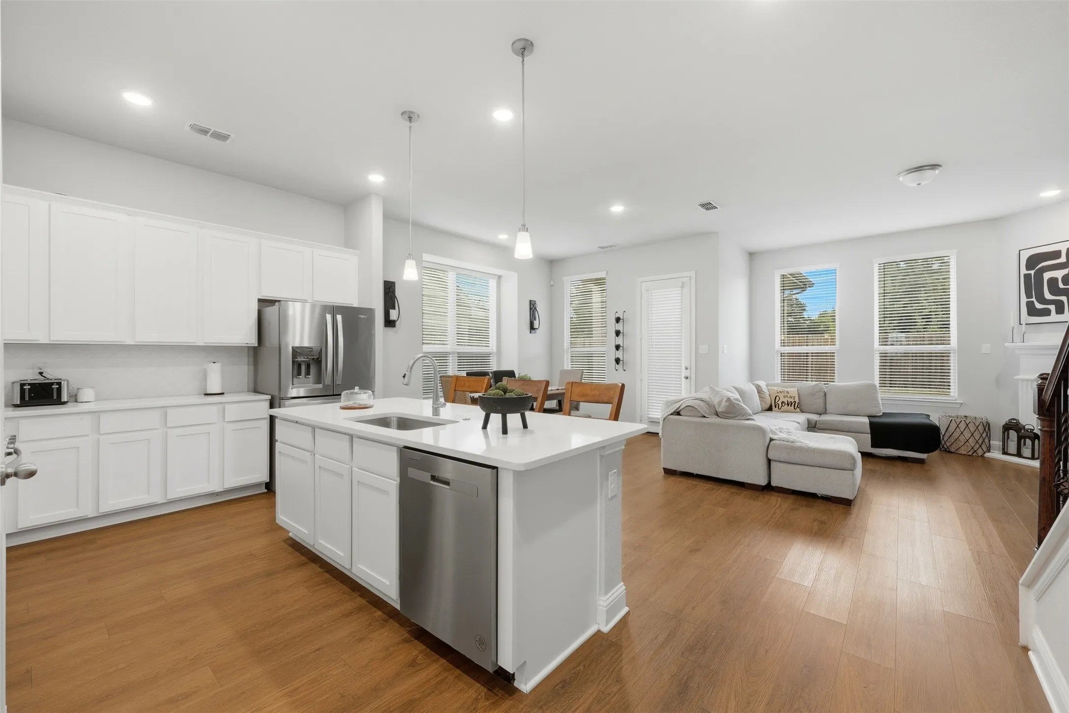 Kitchen featuring an island with sink, stainless steel appliances, pendant lighting, and white cabinetry