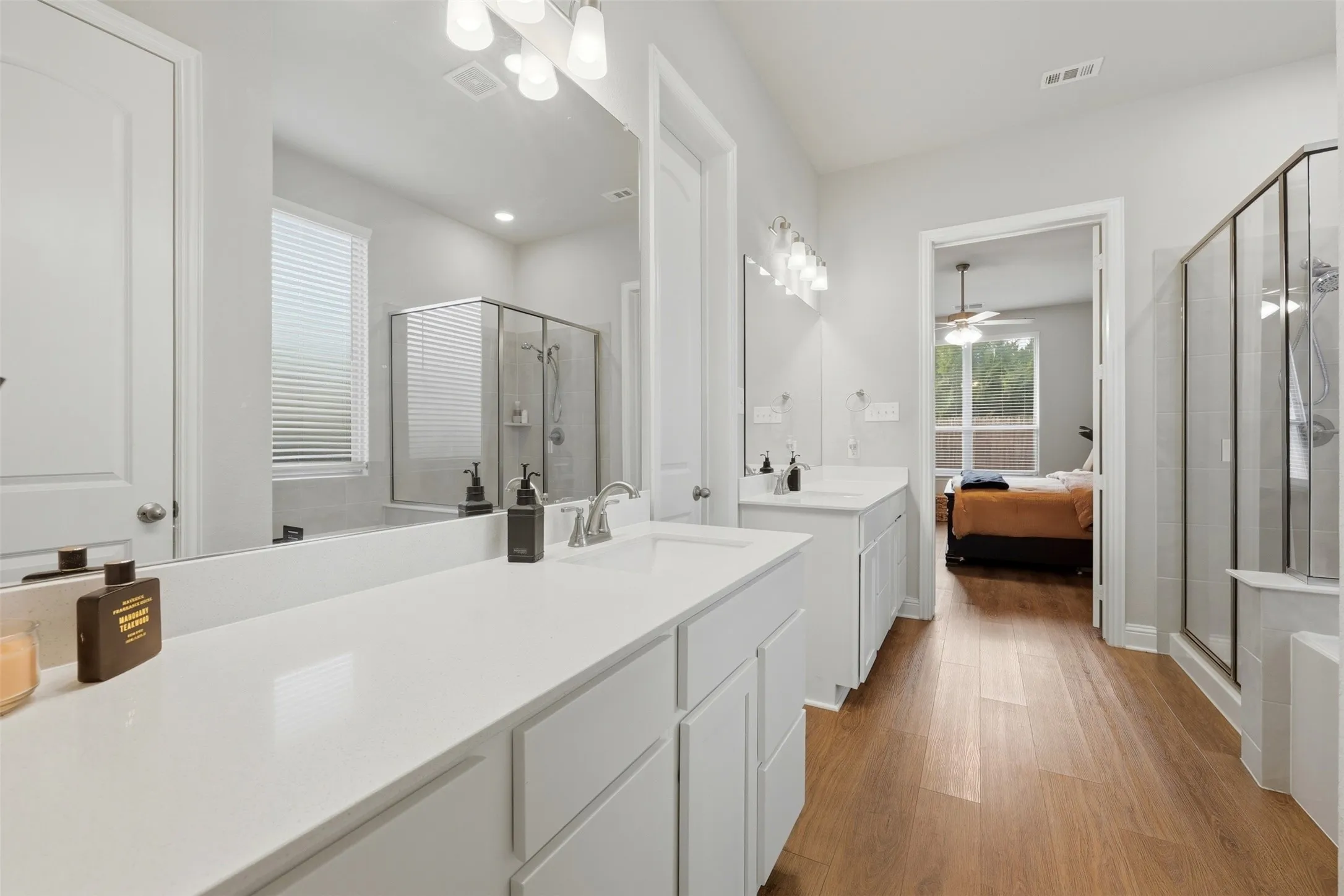 Ensuite bathroom featuring a stall shower, two vanities, light wood-style floors, and a ceiling fan