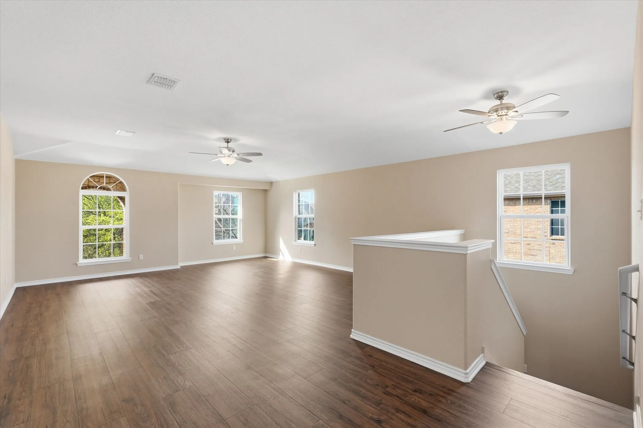 Empty room featuring a ceiling fan, dark wood-style flooring, and plenty of natural light