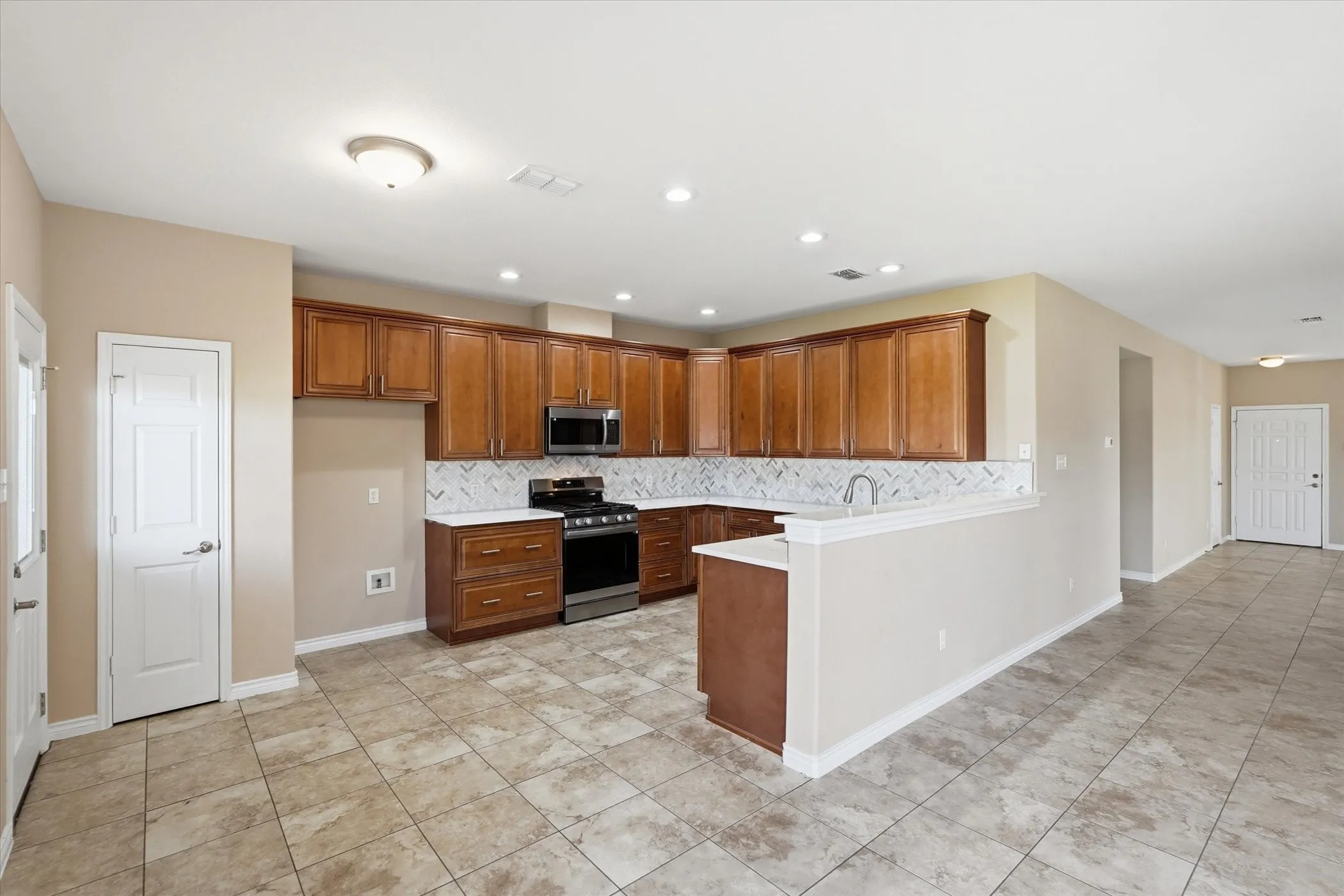 Kitchen with wood finish cabinets, stainless steel appliances, a peninsula, backsplash, and recessed lighting
