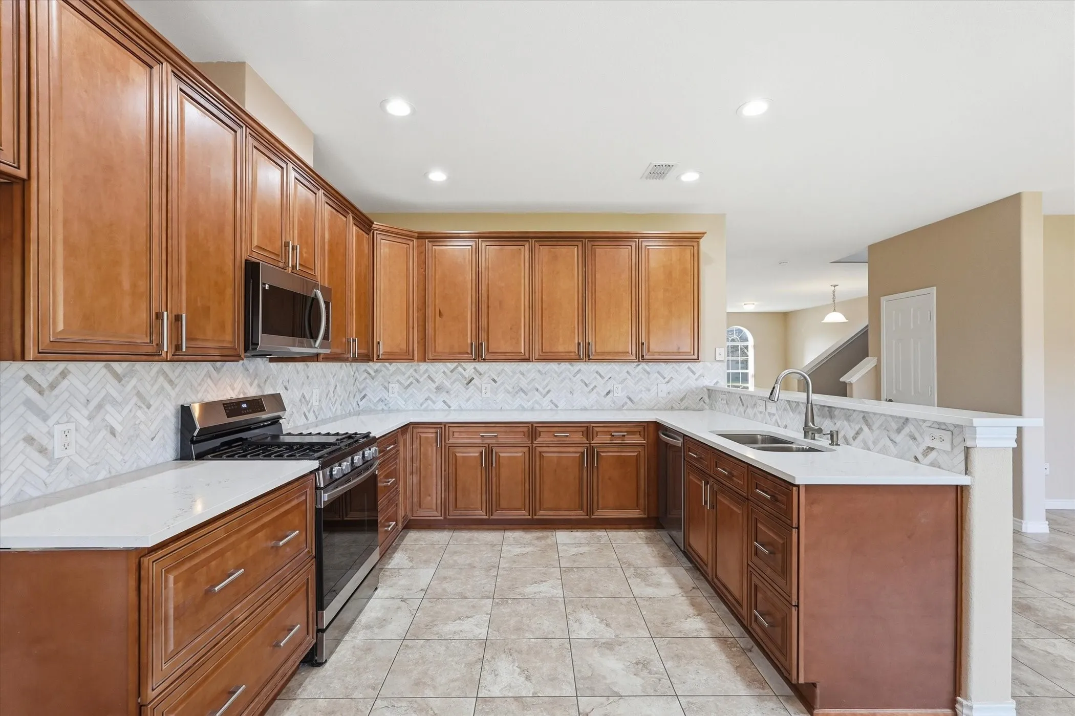 Kitchen featuring stainless steel appliances, wood finish cabinetry, a peninsula, light stone counters, and light tile patterned floors