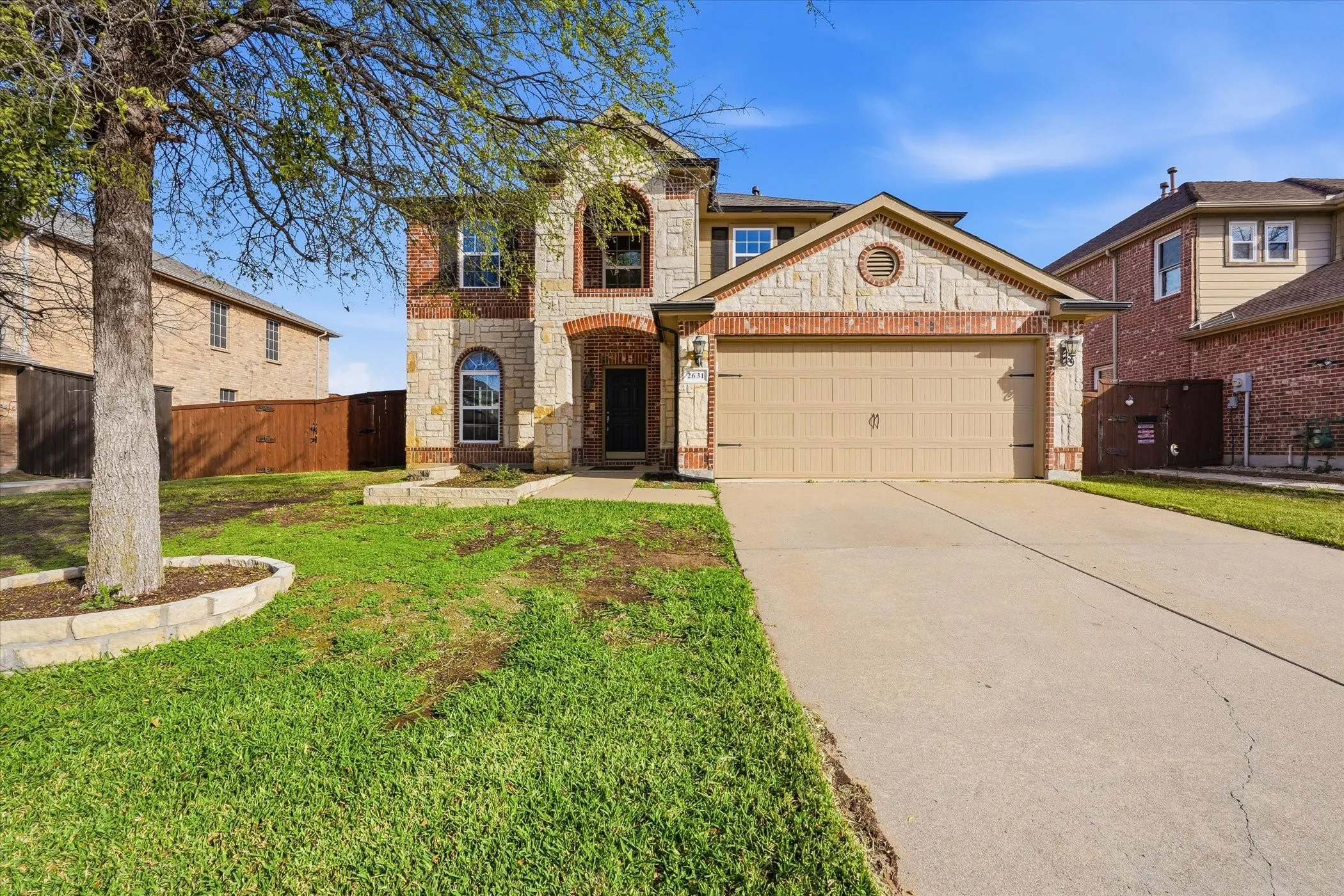 View of front of home with brick siding, a garage, driveway, stone siding, and a gate