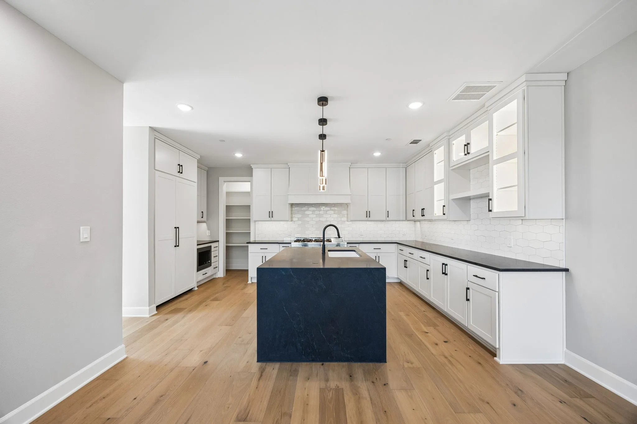 Kitchen with white cabinets, decorative light fixtures, open shelves, and a center island with sink