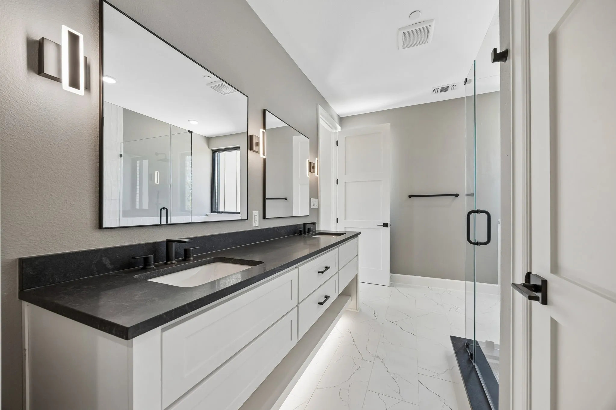 Bathroom with double vanity, light marble finish floors, and a shower stall