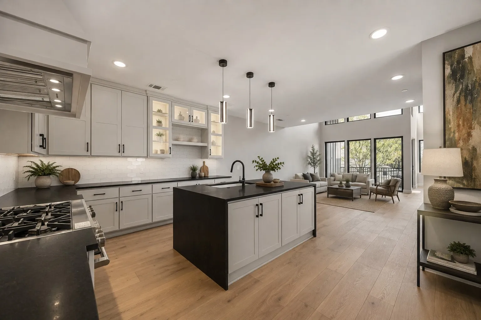 Open-concept kitchen featuring light-toned cabinetry, dark countertops, a central island, and modern pendant lighting