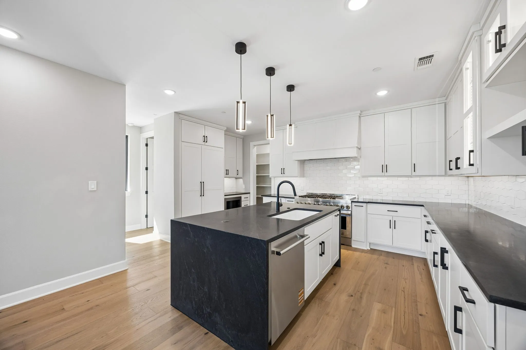 Kitchen with an island with sink, stainless steel appliances, white cabinetry, and light wood finished floors