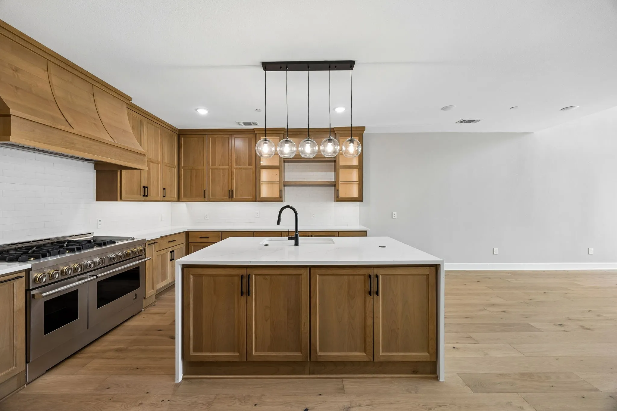 Kitchen with light wood-type flooring, range with two ovens, a kitchen island with sink, light stone countertops, and wood finish cabinets