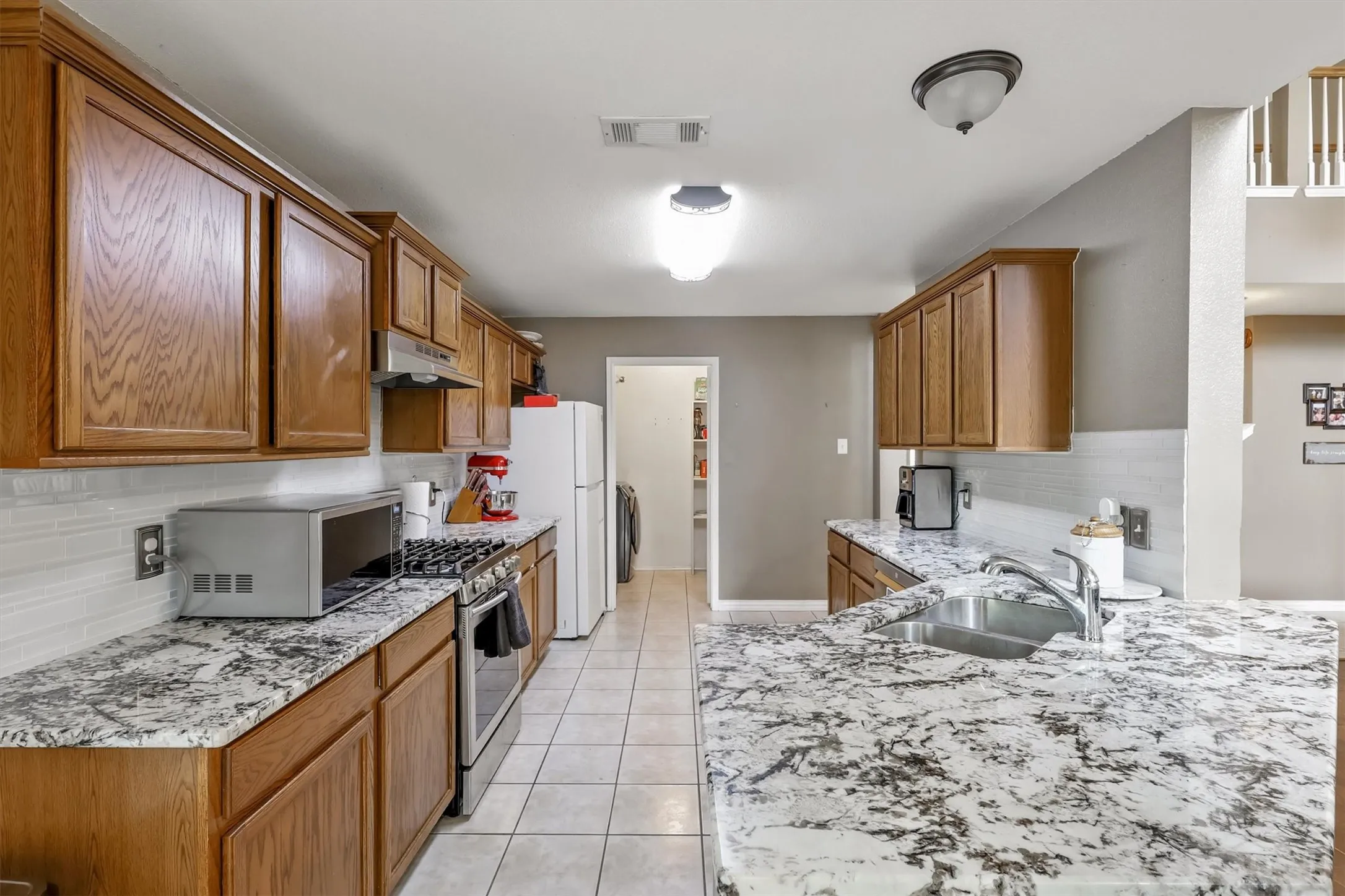 Kitchen featuring tasteful backsplash, under cabinet range hood, light tile patterned floors, brown cabinetry, and freestanding refrigerator