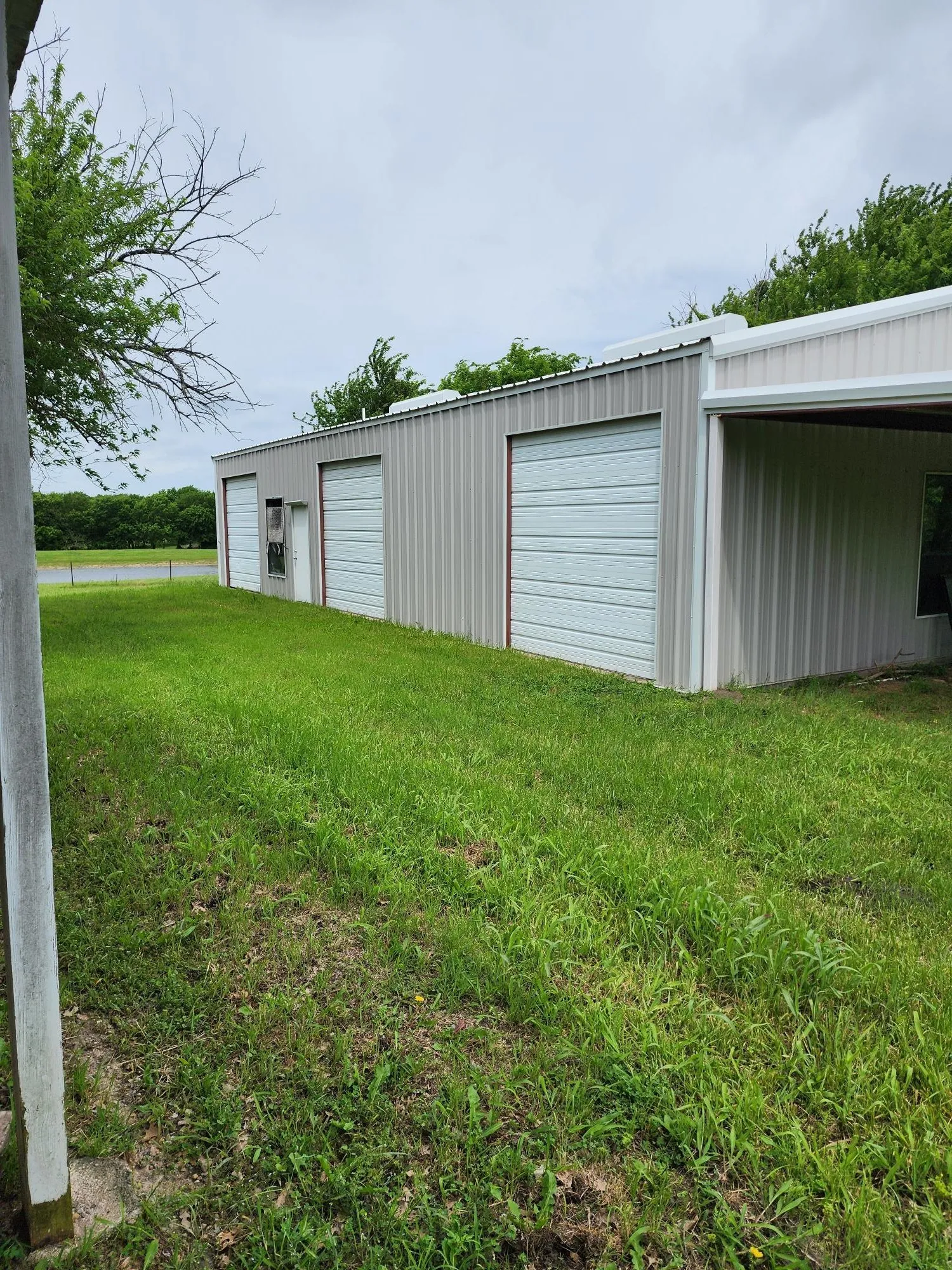 Industrial-style building featuring corrugated metal siding, multiple roll-up garage doors, a pedestrian entrance, and an attached covered carport