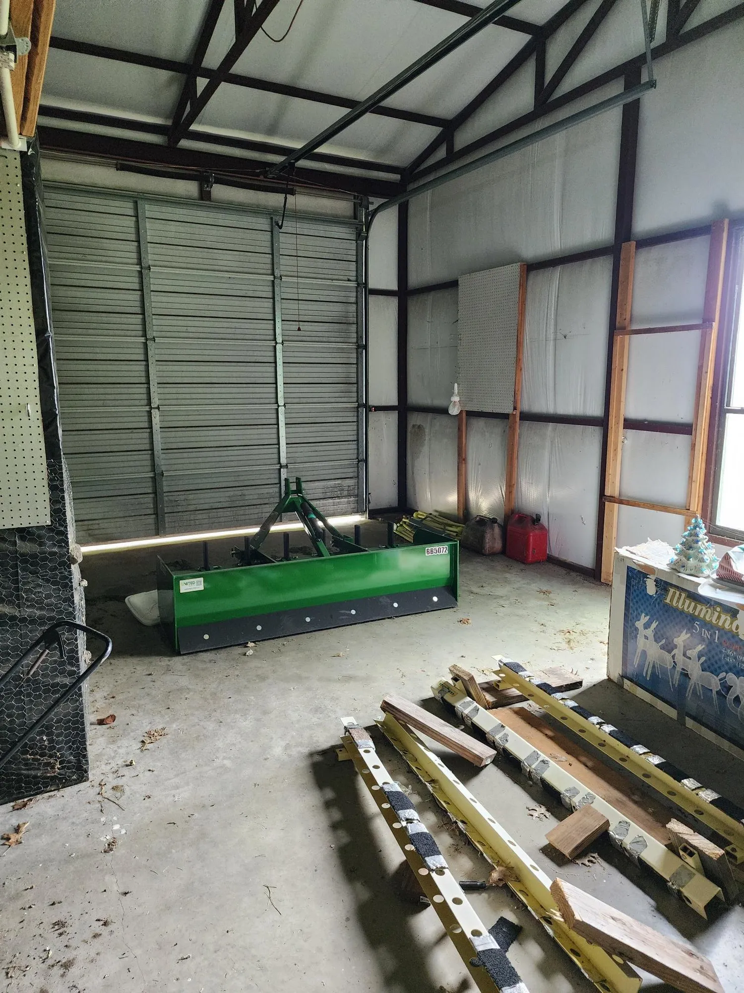 Spacious garage with a roll-up door, exposed metal structural beams, white insulated wall panels, and a concrete floor