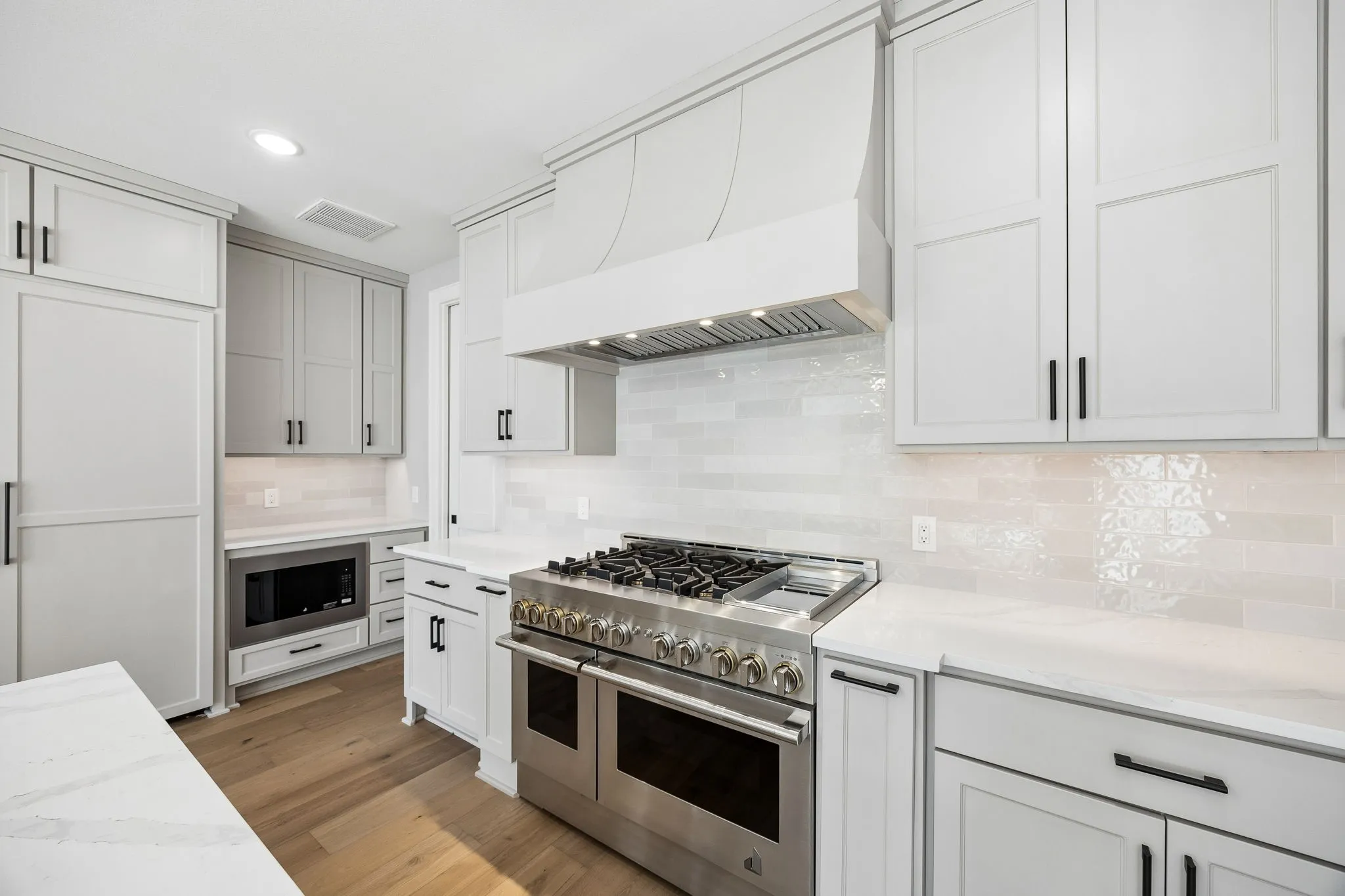 Kitchen with stainless steel appliances, recessed lighting, backsplash, light wood-type flooring, and light stone countertops