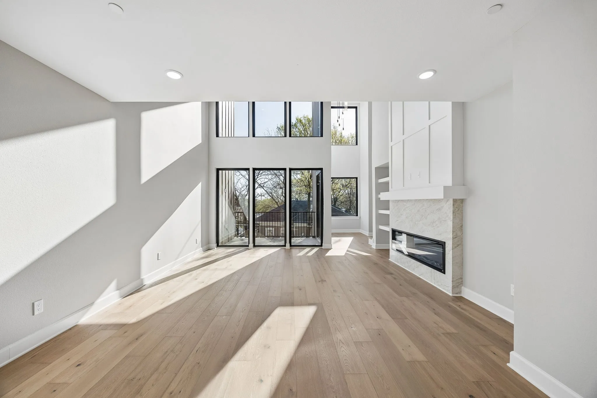 Unfurnished living room featuring light wood-type flooring, a tiled fireplace, a high ceiling, and recessed lighting