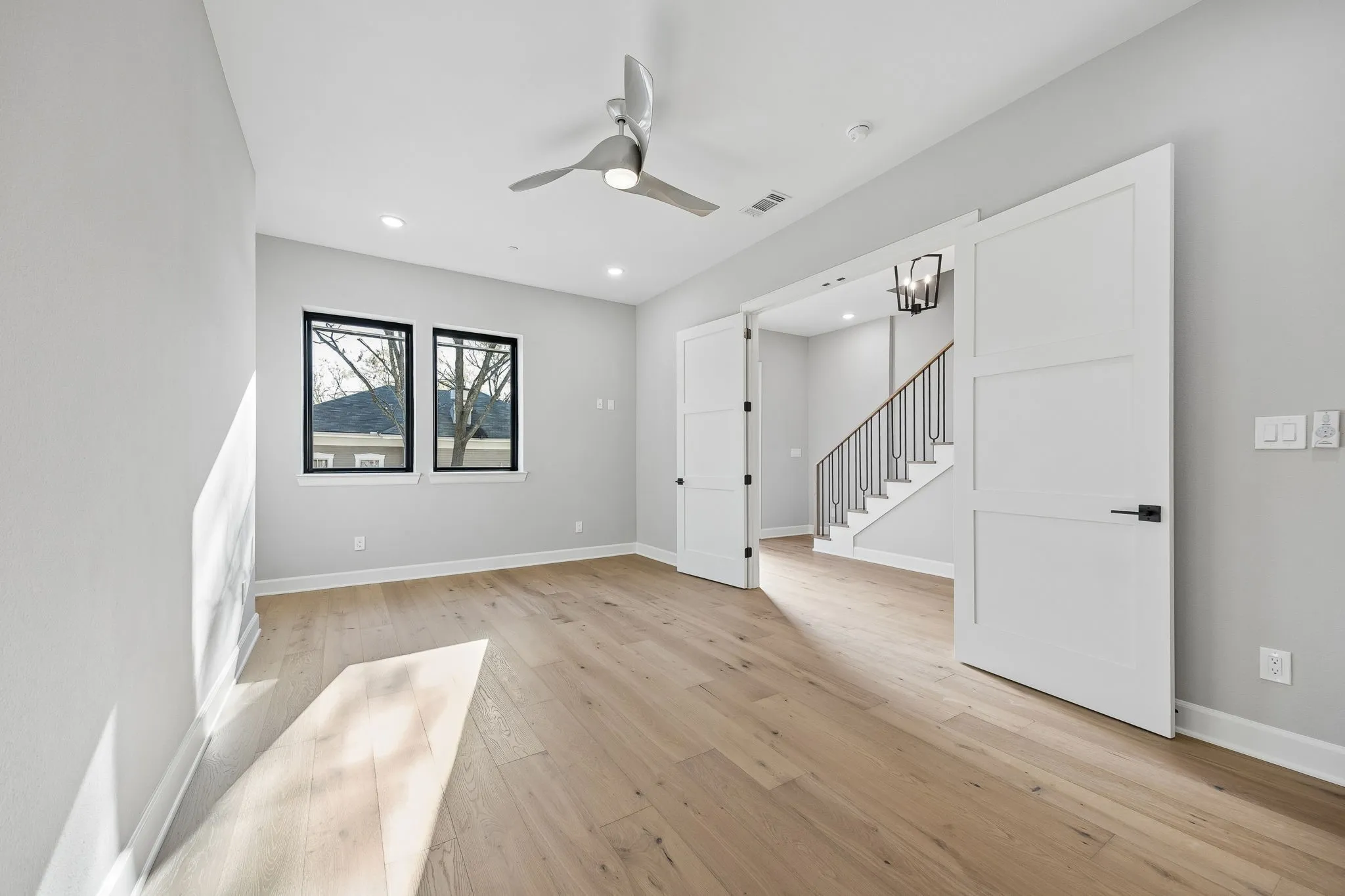 Empty room featuring light wood-type flooring, a ceiling fan, hanging lights, and a barn door