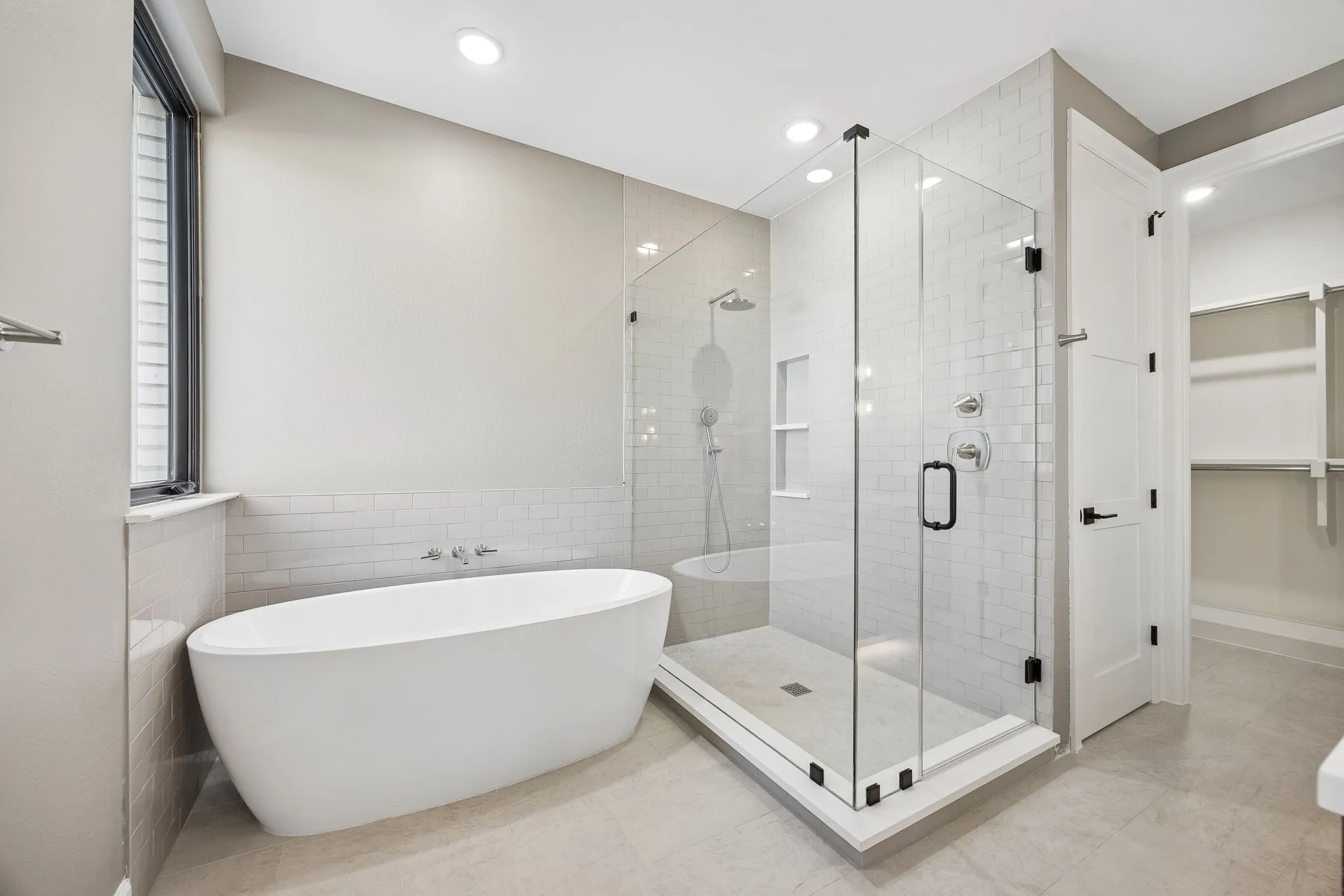 Bathroom with a walk in closet, a freestanding tub, a shower stall, tile walls, and recessed lighting