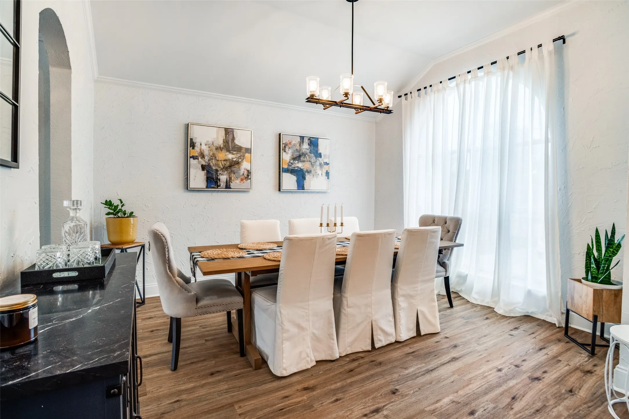 Dining room featuring wood finished floors, a textured wall, suspended lighting, lofted ceiling, and ornamental molding