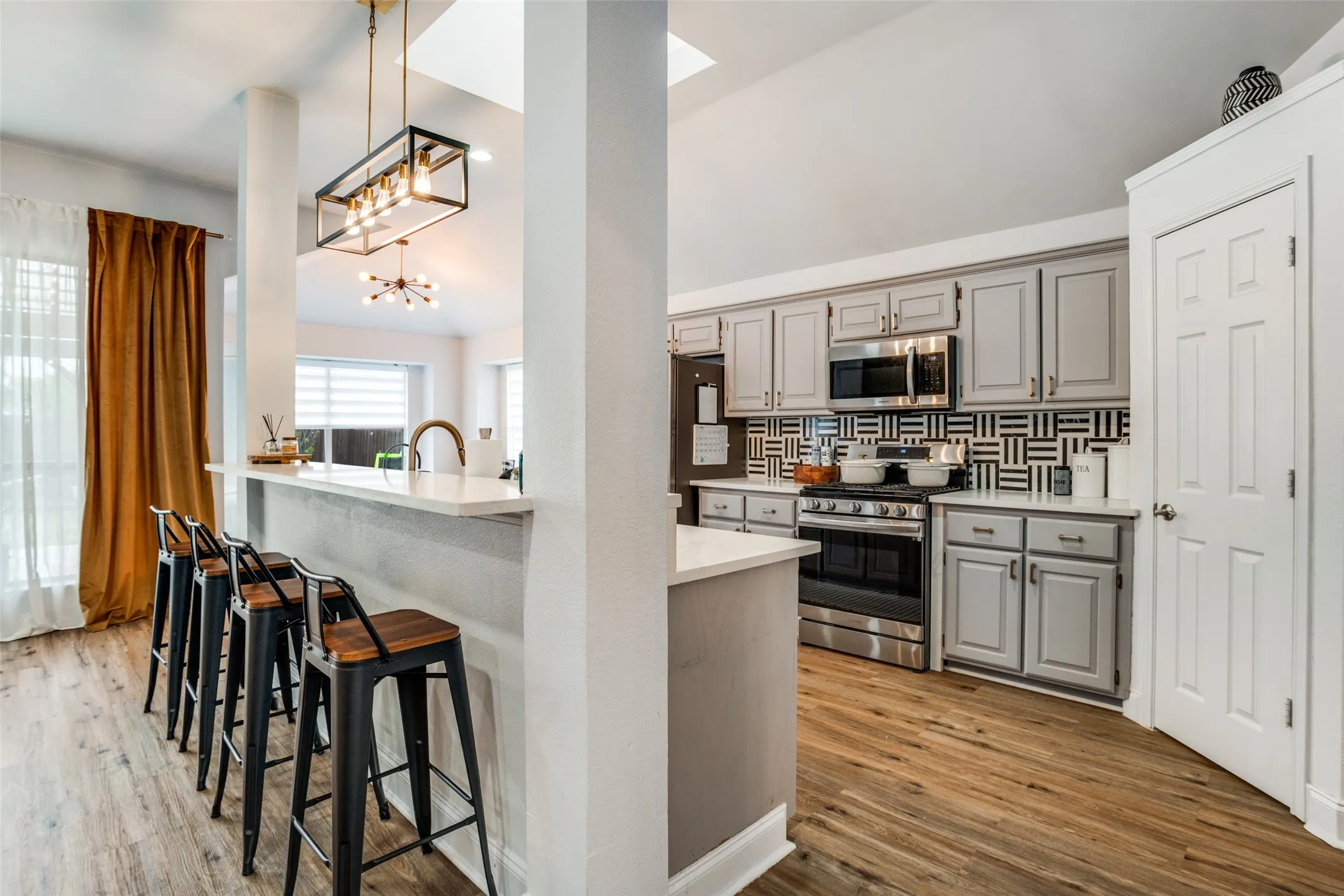 Kitchen with gray cabinets, stainless steel appliances, dark wood-style flooring, a breakfast bar, and tasteful backsplash