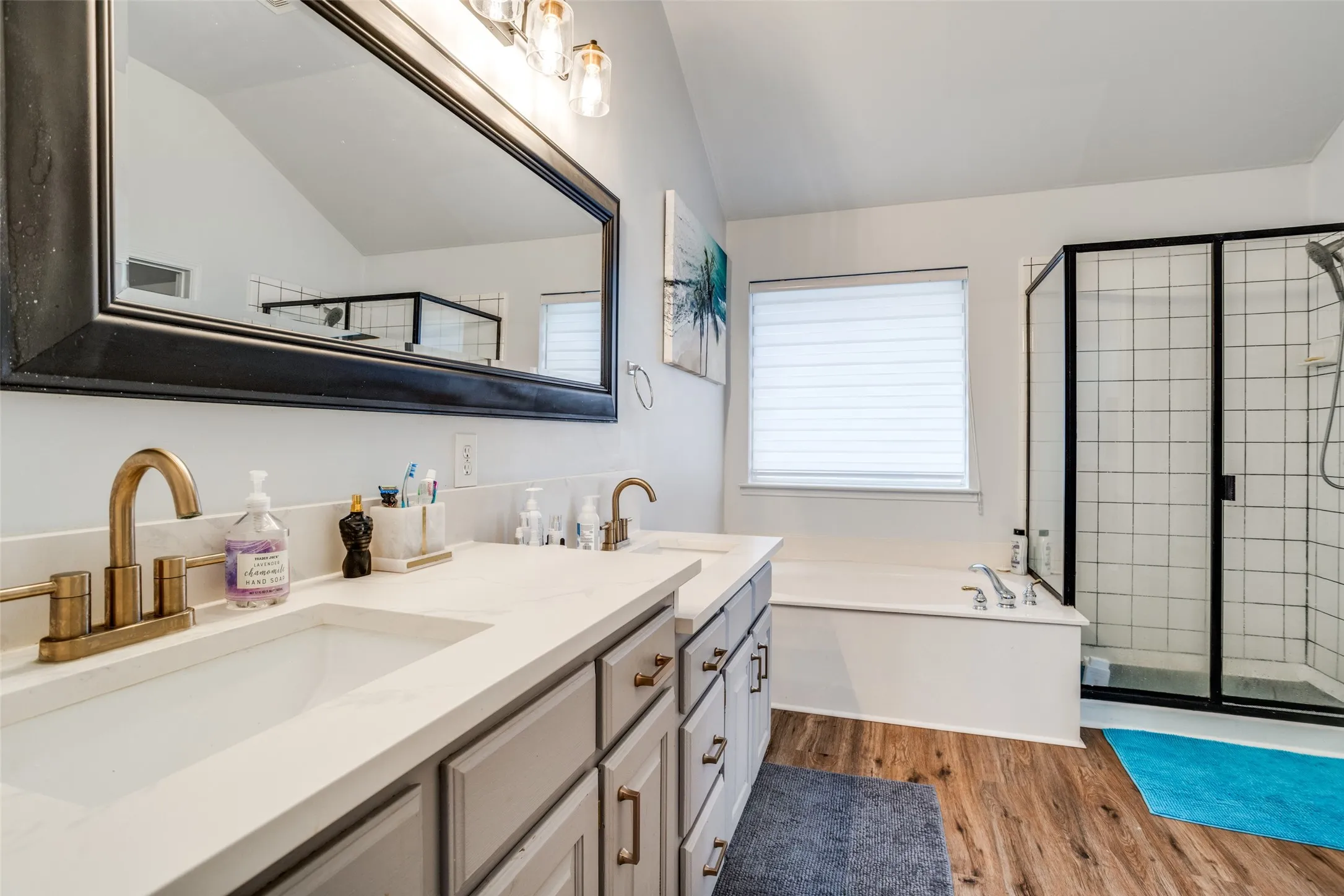 Bathroom with double vanity, a stall shower, a garden tub, dark wood-style floors, and lofted ceiling