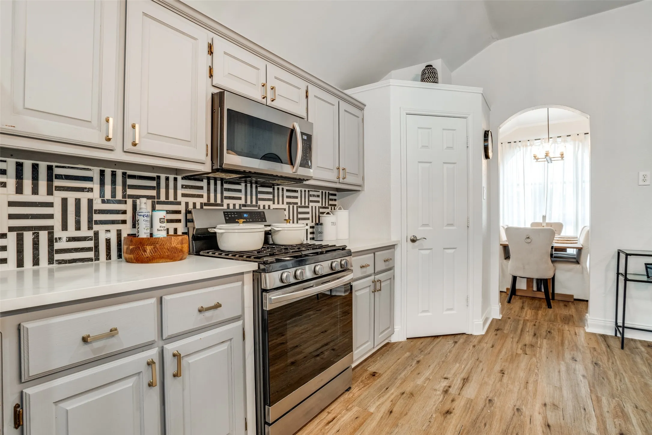 Kitchen with stainless steel appliances, light countertops, decorative backsplash, arched walkways, and vaulted ceiling