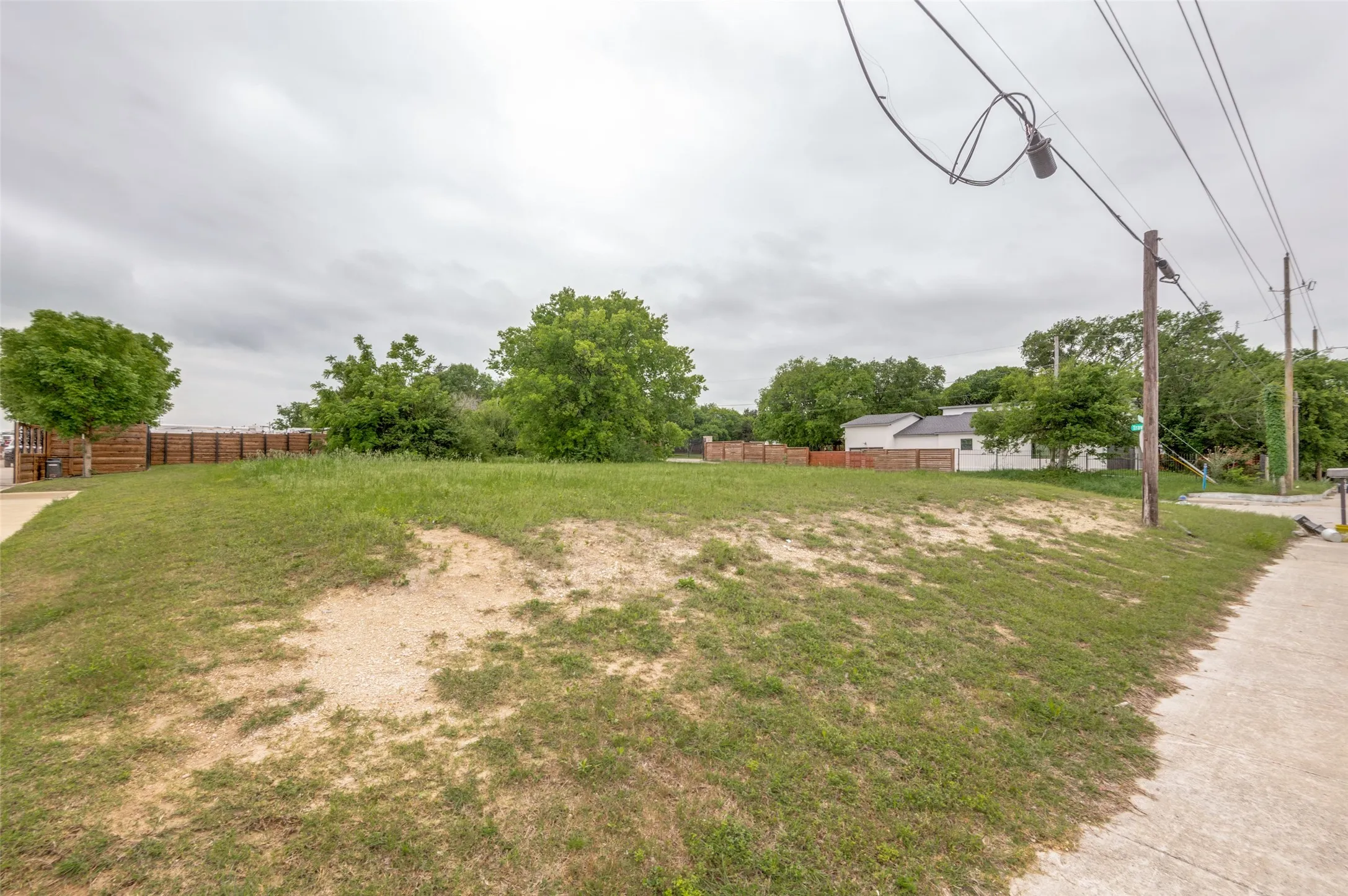 Expansive lot featuring a grass and dirt surface, mature trees, and a perimeter fence
