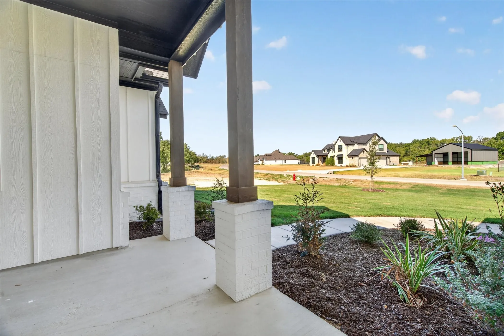 Covered front porch with square columns featuring a white brick base, white vertical siding, and dark soffit