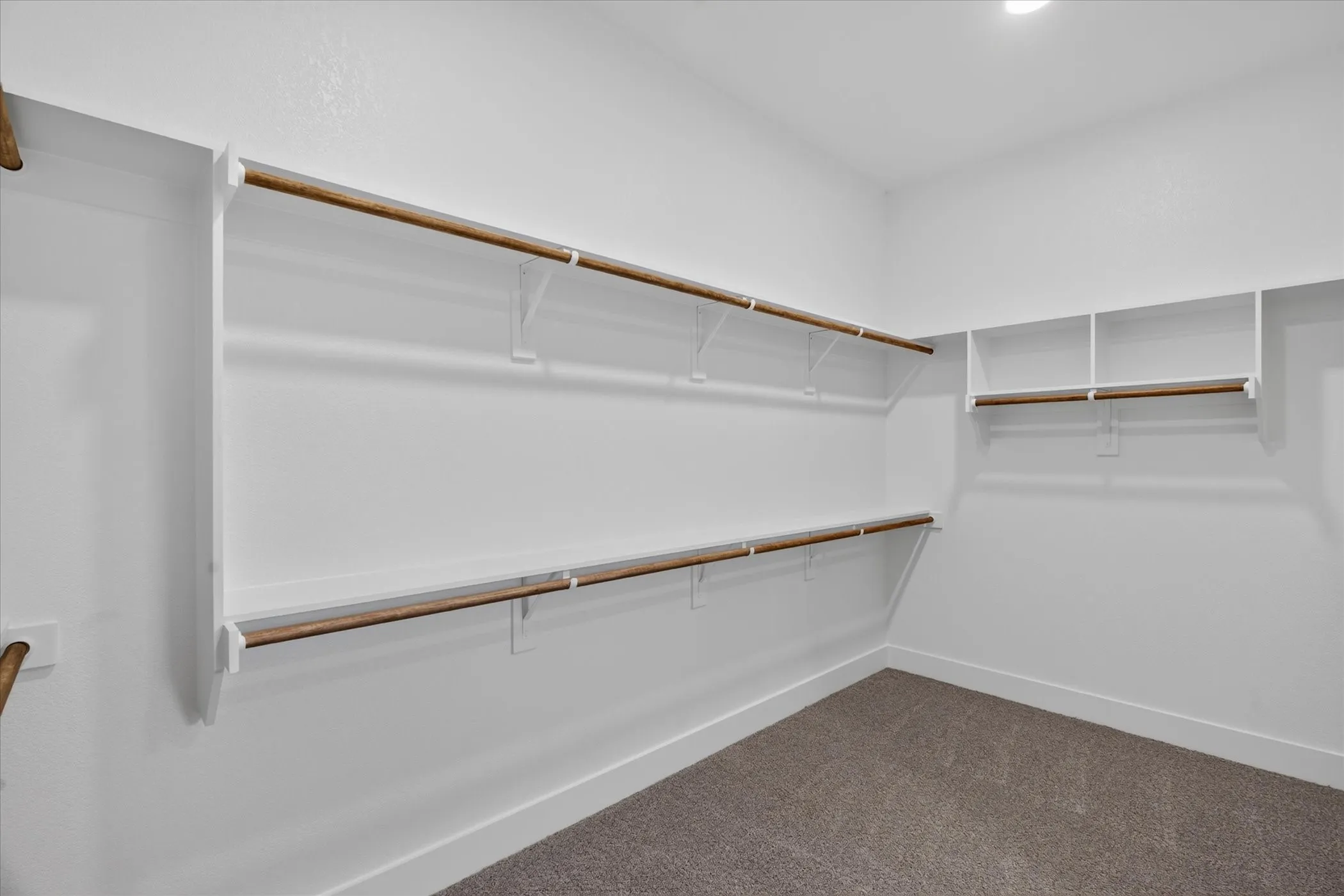 Recessed lighting illuminates a carpeted walk-in closet featuring multiple hanging rods and built-in shelving