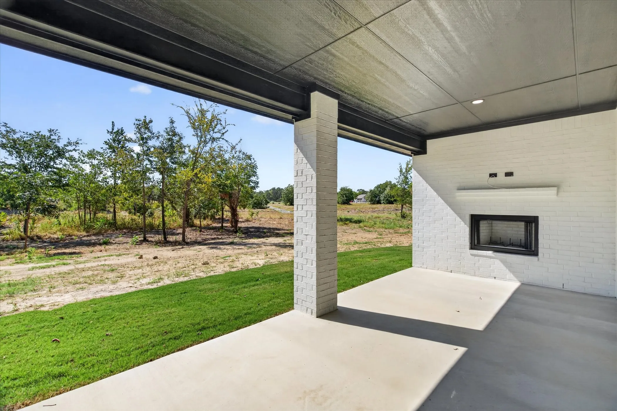 Covered patio with a concrete surface, white brick exterior wall, built-in fireplace, and recessed lighting