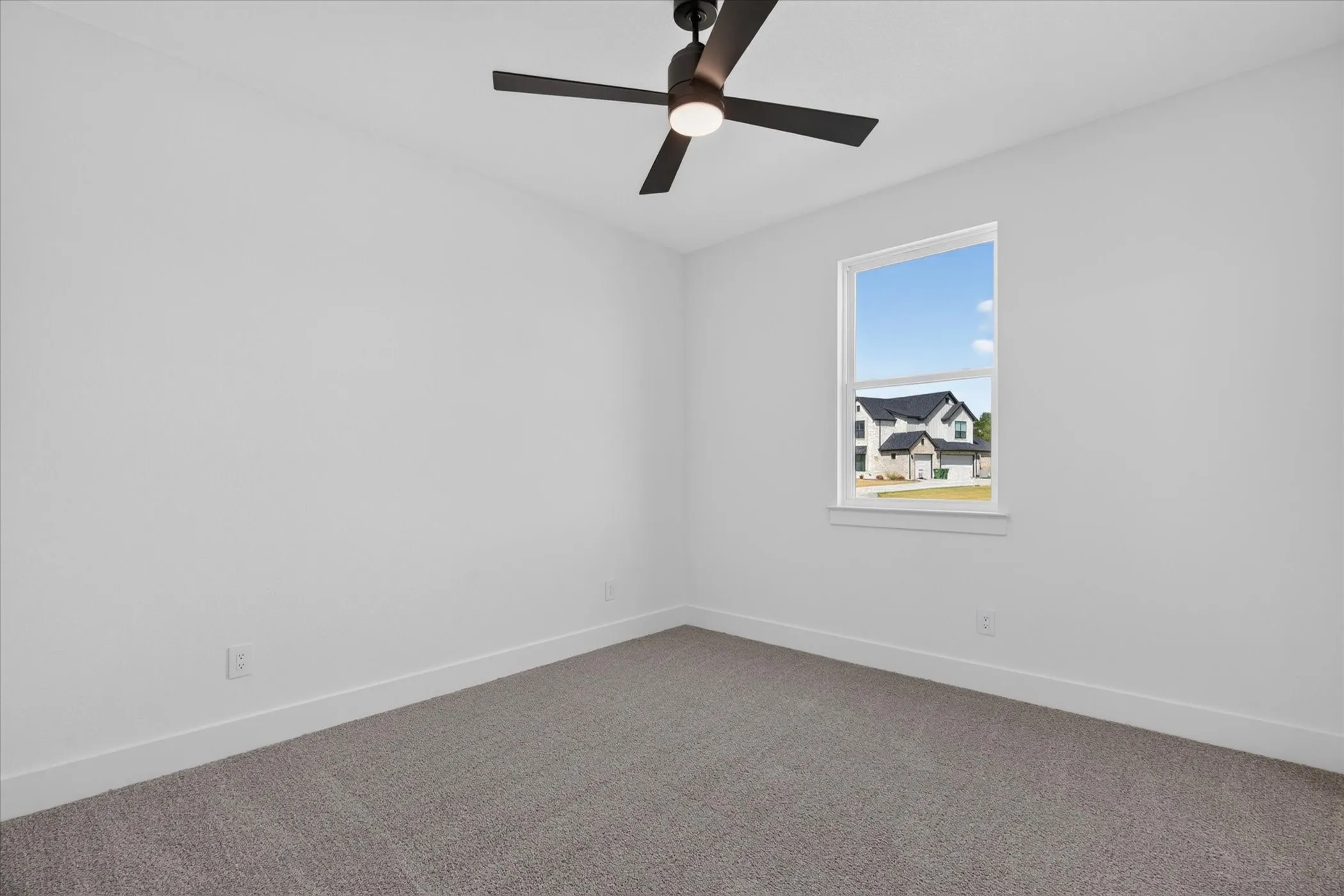 Spacious room featuring white walls, gray carpeting, a single window, and a ceiling fan with integrated lighting