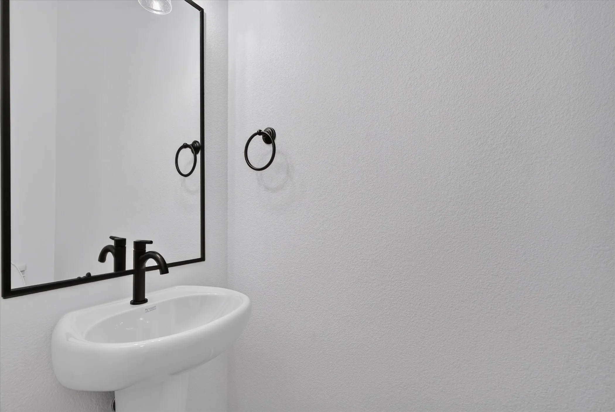 Pedestal sink with a matte black faucet and mirror
