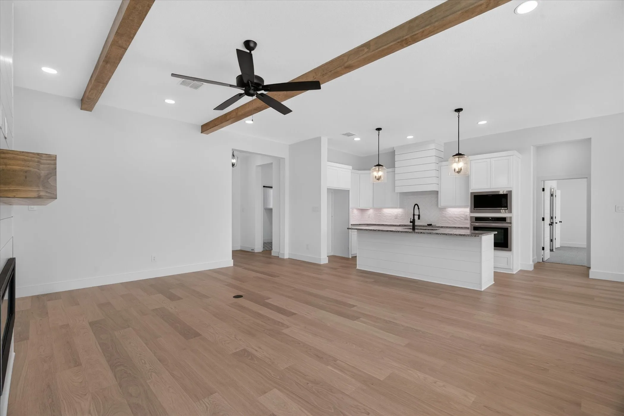 Open-concept living space featuring wood-finish flooring, exposed ceiling beams, recessed lighting, and a modern kitchen