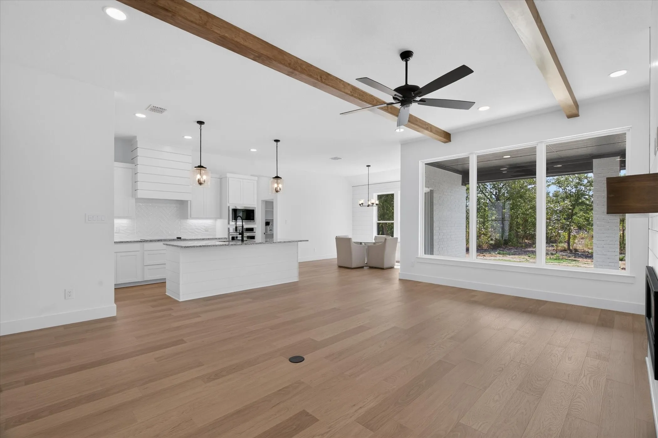 Wood-finish flooring, exposed wood ceiling beams, white cabinetry, a kitchen island with seating, and large windows
