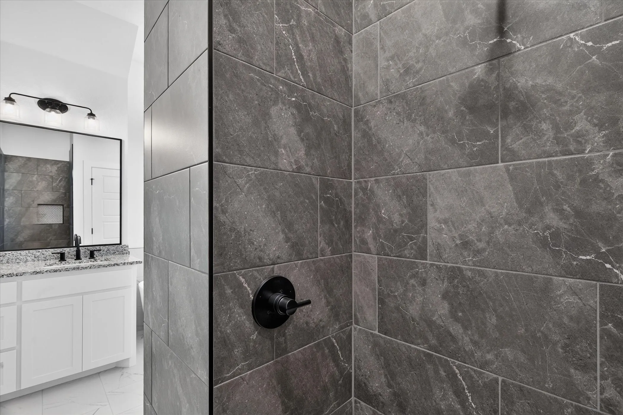Shower featuring dark grey tile with subtle veining and a matte black shower control