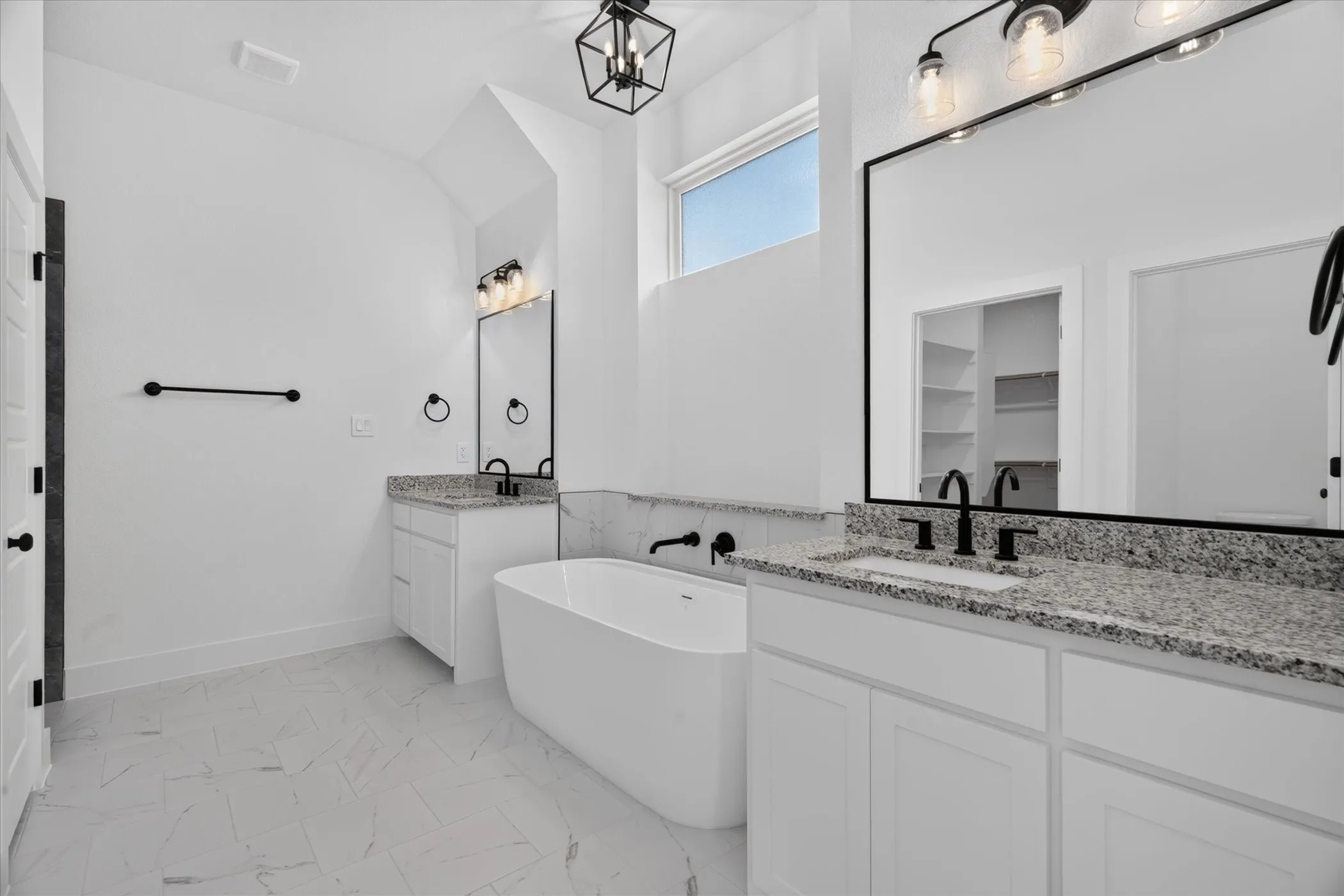 Freestanding soaking tub, dual vanities with granite countertops, black fixtures, rectangular mirrors, and vaulted ceiling with a geometric light fixture